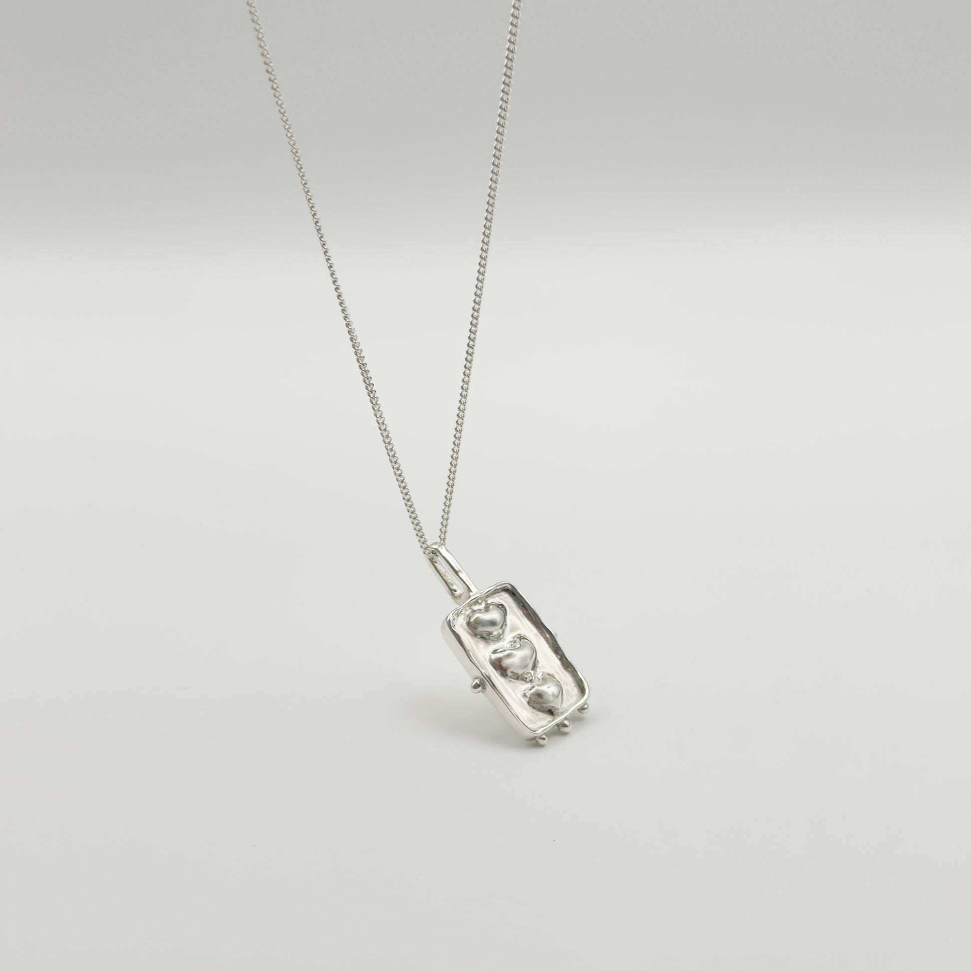 Angled front view of the Self-Compassion textured silver pendant on a curb chain, pictured on a light plain background.
