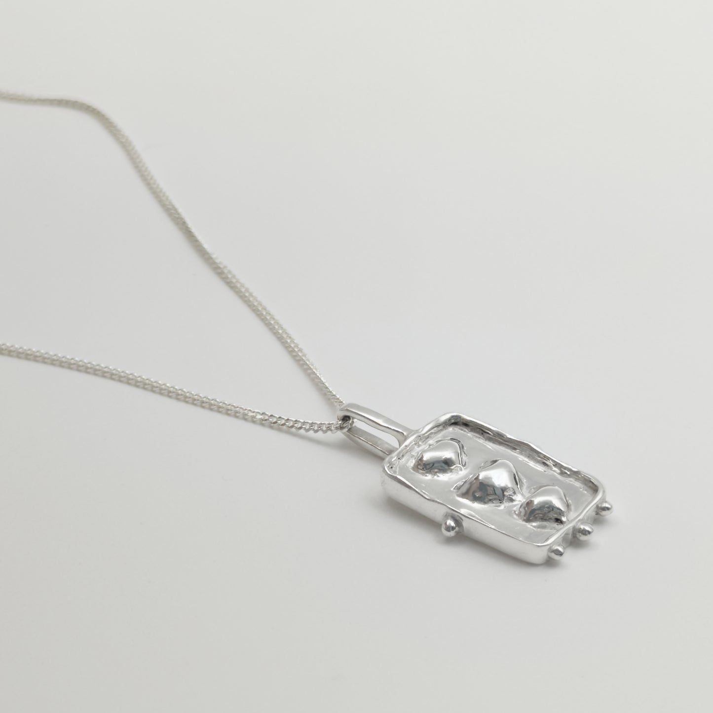 Close-up view of the Self-Compassion textured silver pendant on a curb chain, pictured on a light plain background.