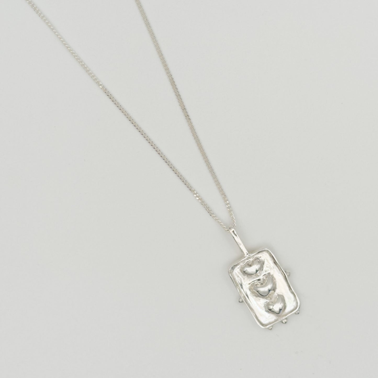 Close-up top view of the Self-Compassion textured silver pendant on a curb chain, pictured on a light plain background.