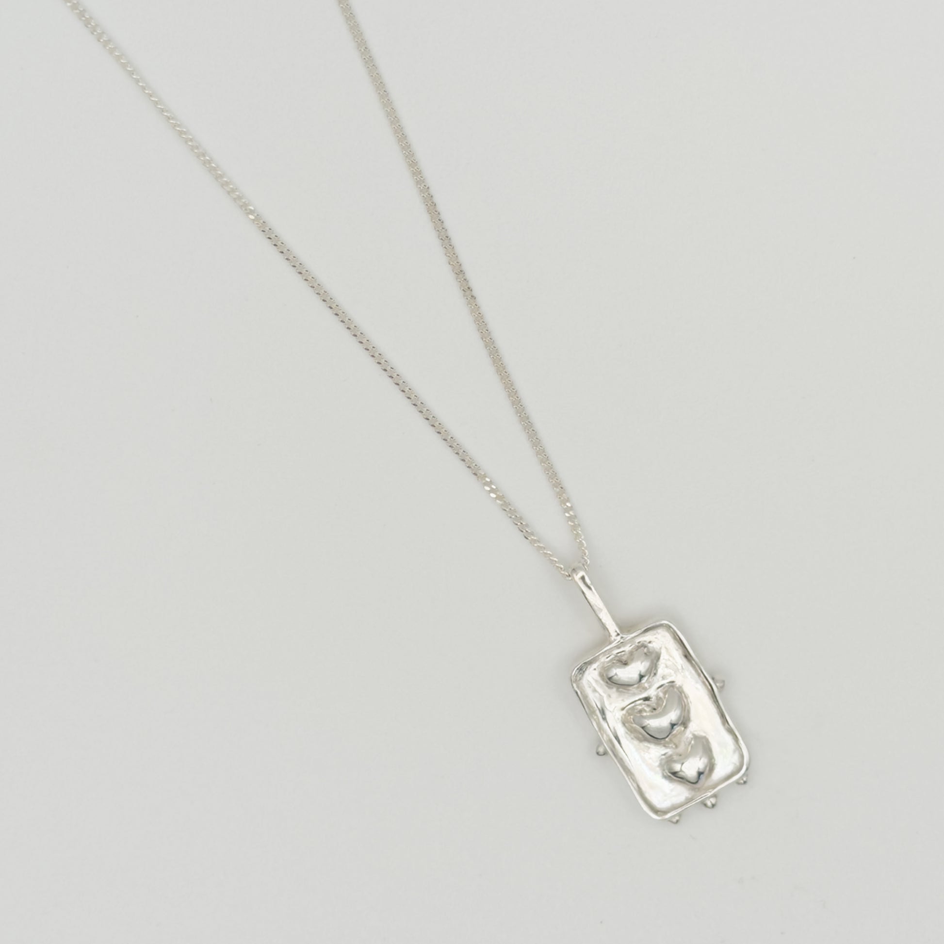 Close-up top view of the Self-Compassion textured silver pendant on a curb chain, pictured on a light plain background.