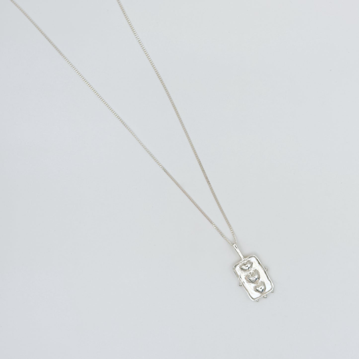Top view of the Self-Compassion textured silver pendant on a curb chain, pictured on a light plain background.