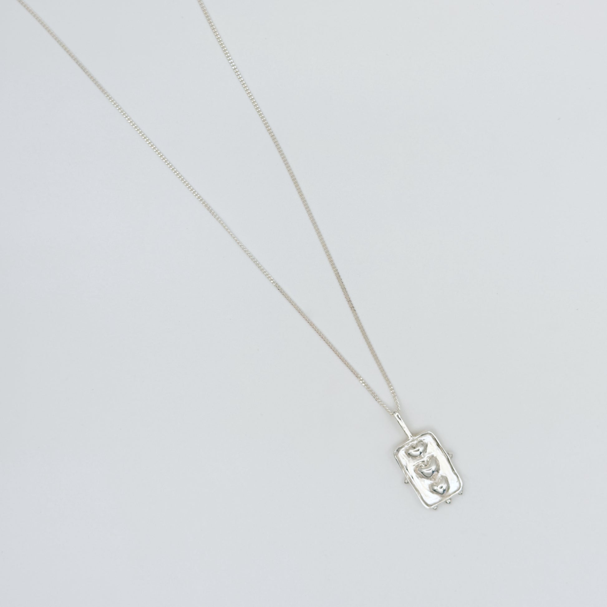 Top view of the Self-Compassion textured silver pendant on a curb chain, pictured on a light plain background.
