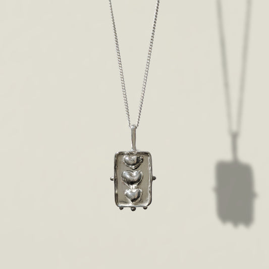 Front view of the Self-Compassion textured silver pendant on a curb chain, pictured on a light plain background.