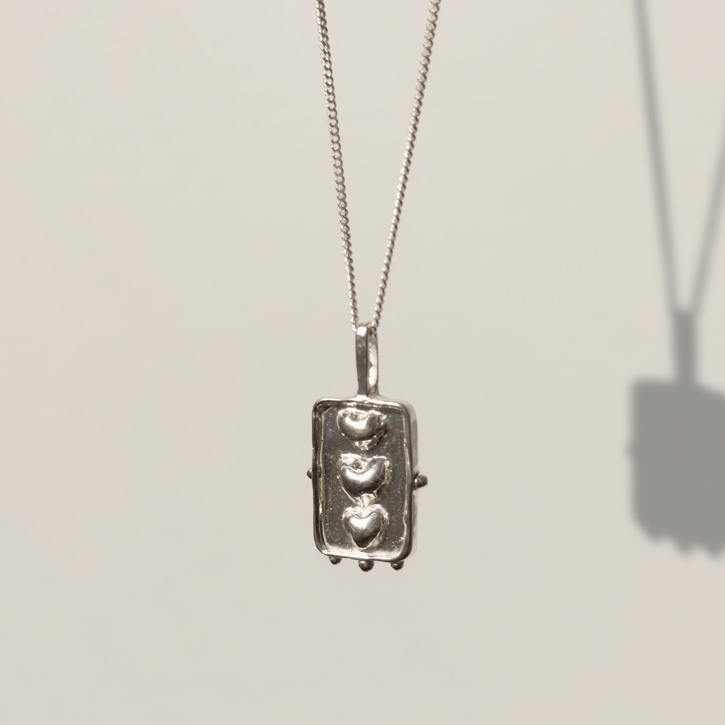 Angled front view of the Self-Compassion textured silver pendant on a curb chain, pictured on a light plain background.