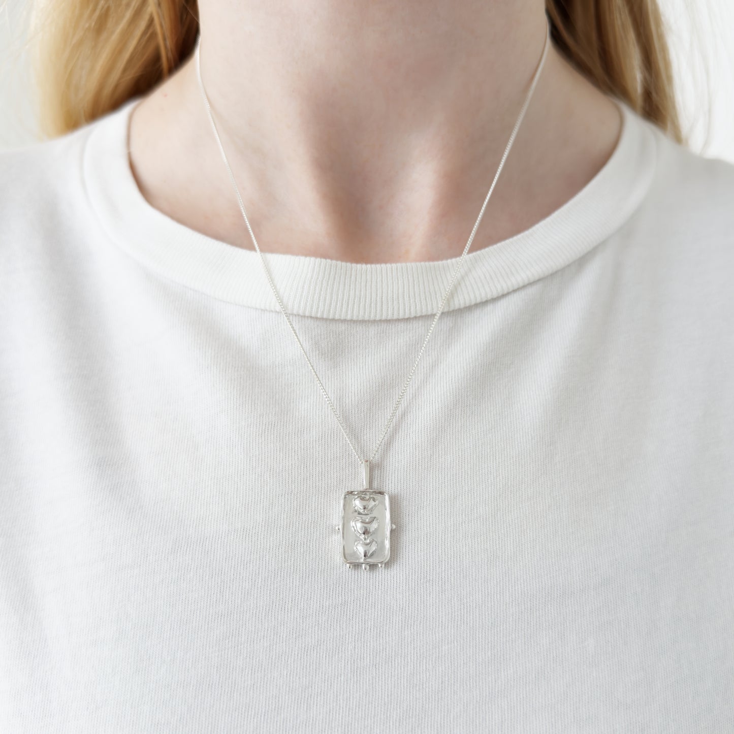 Self-Compassion textured silver pendant on a curb chain. Pictured on a person wearing a white top.