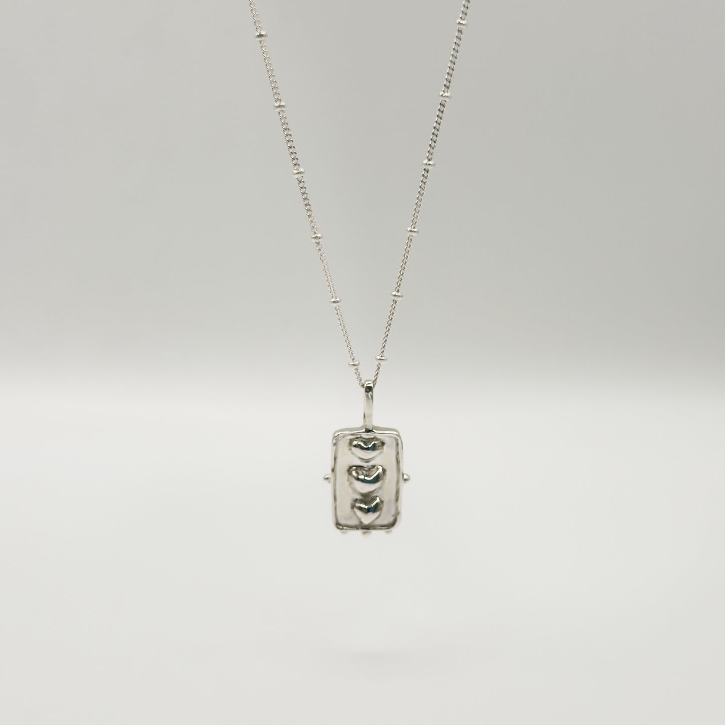 Front view of the Self-Compassion textured silver pendant on a satellite chain, pictured on a light plain background.