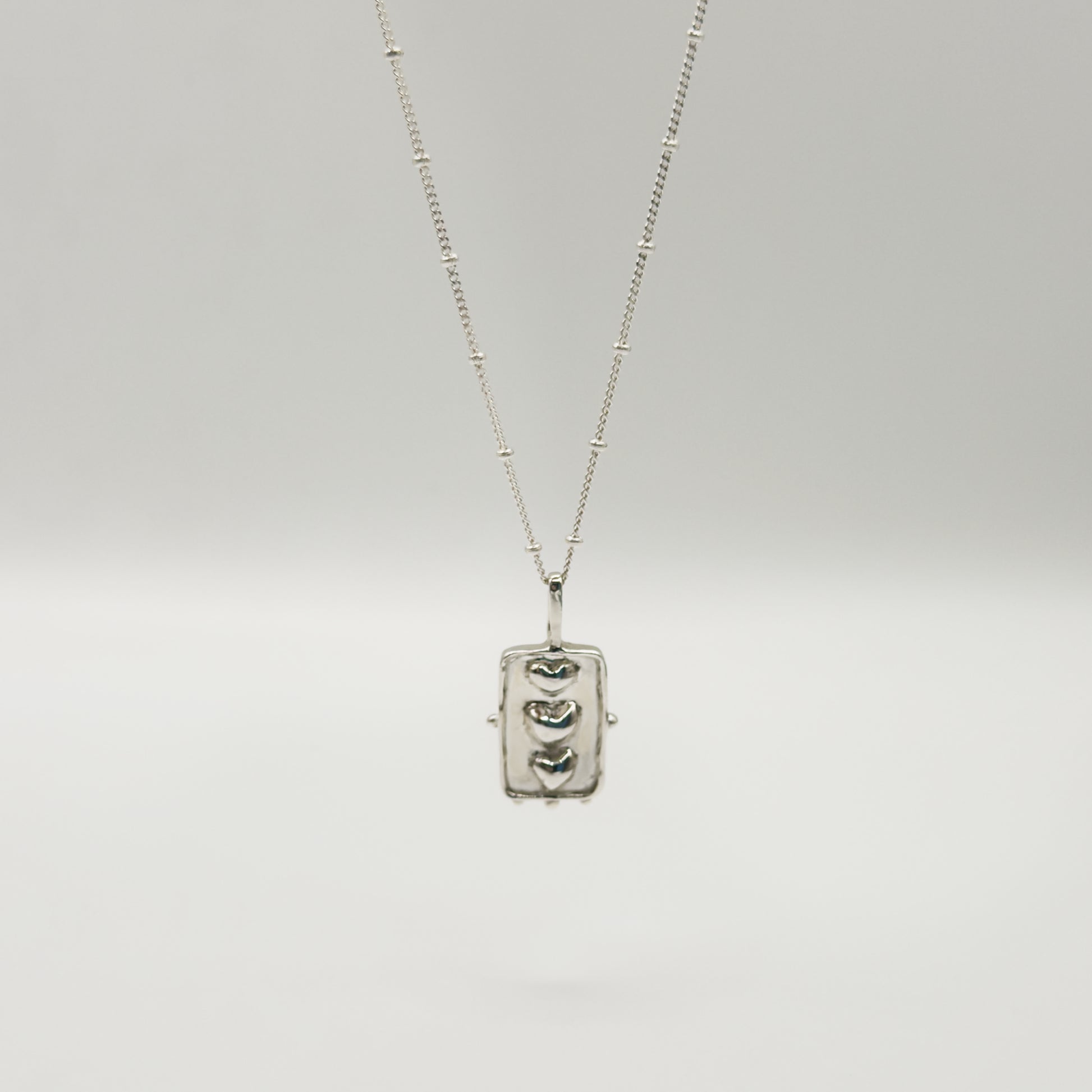 Front view of the Self-Compassion textured silver pendant on a satellite chain, pictured on a light plain background.