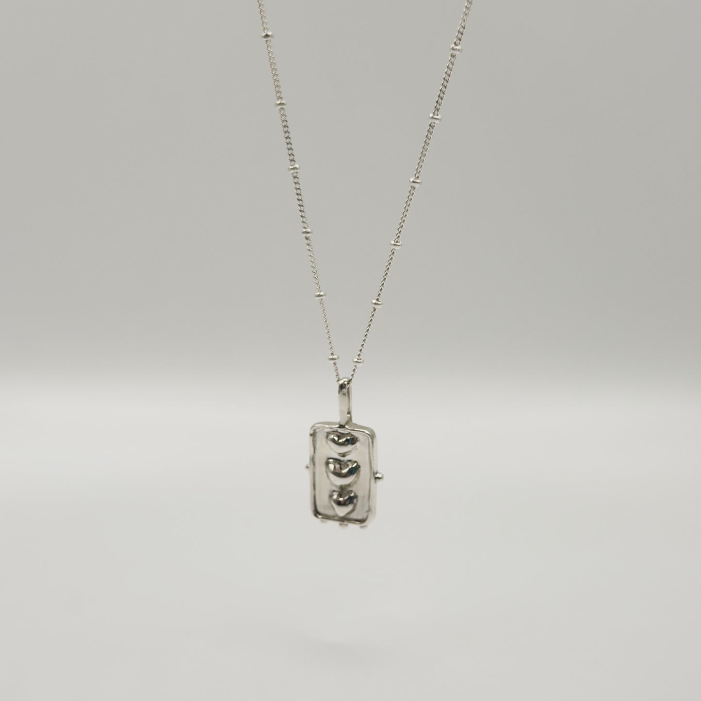 Angled front view of the Self-Compassion textured silver pendant on a satellite chain, pictured on a light plain background.
