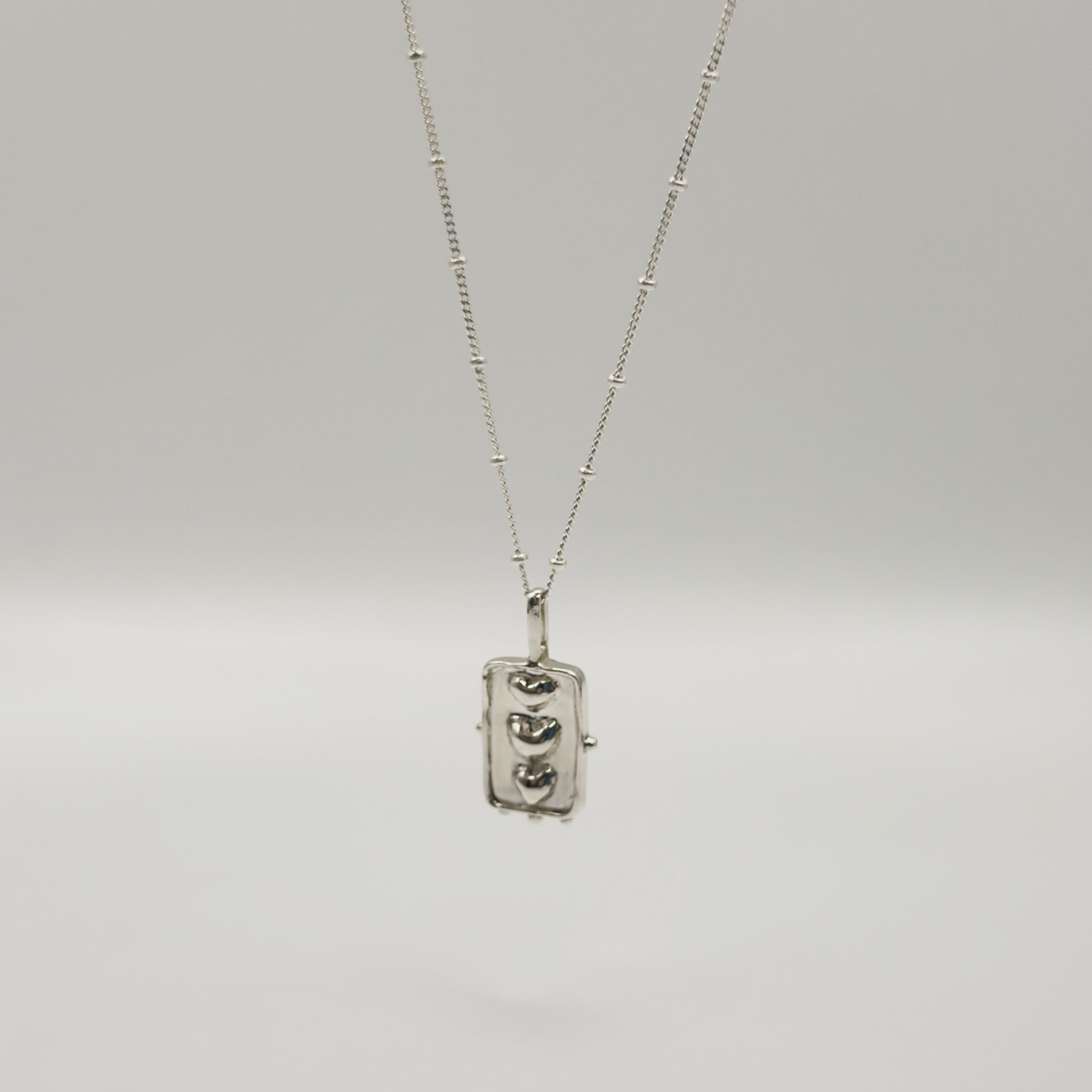 Angled front view of the Self-Compassion textured silver pendant on a satellite chain, pictured on a light plain background.