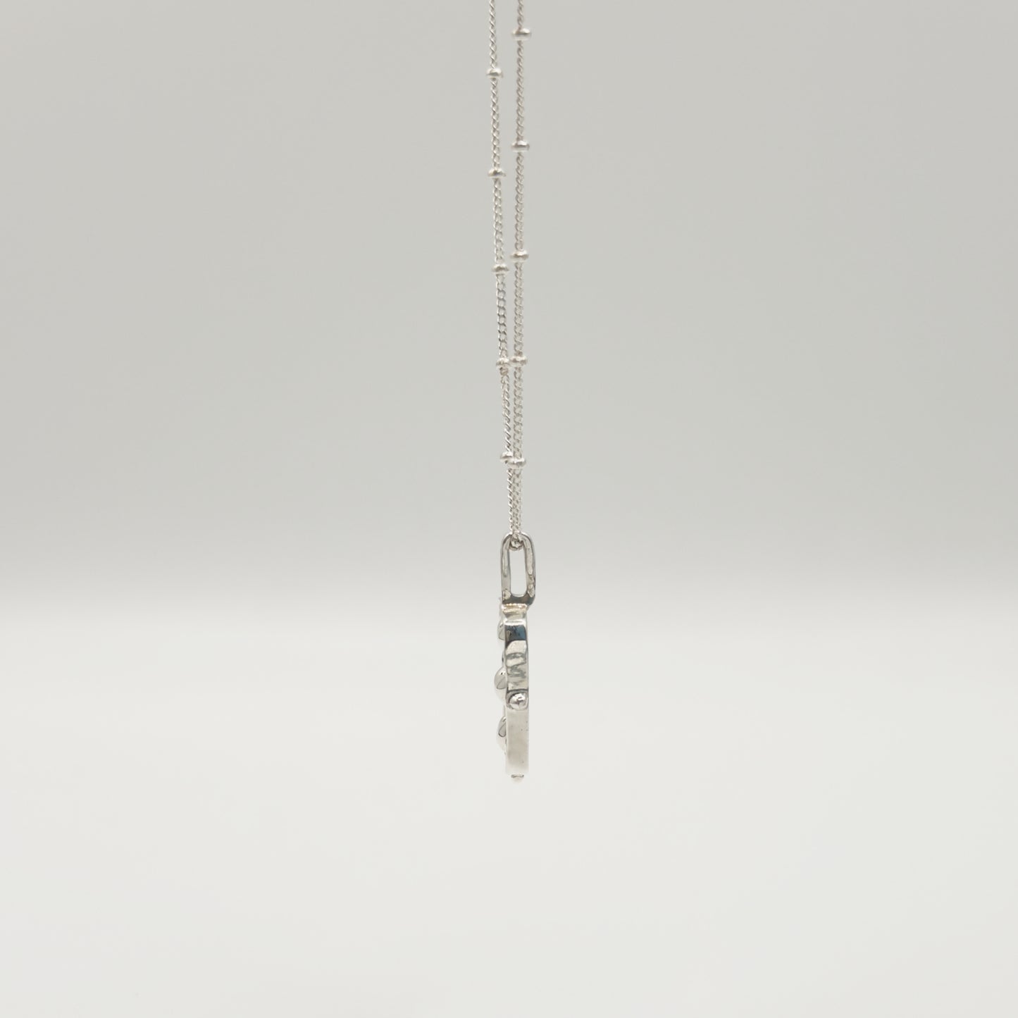 Side view of the Self-Compassion textured silver pendant on a satellite chain, pictured on a light plain background.
