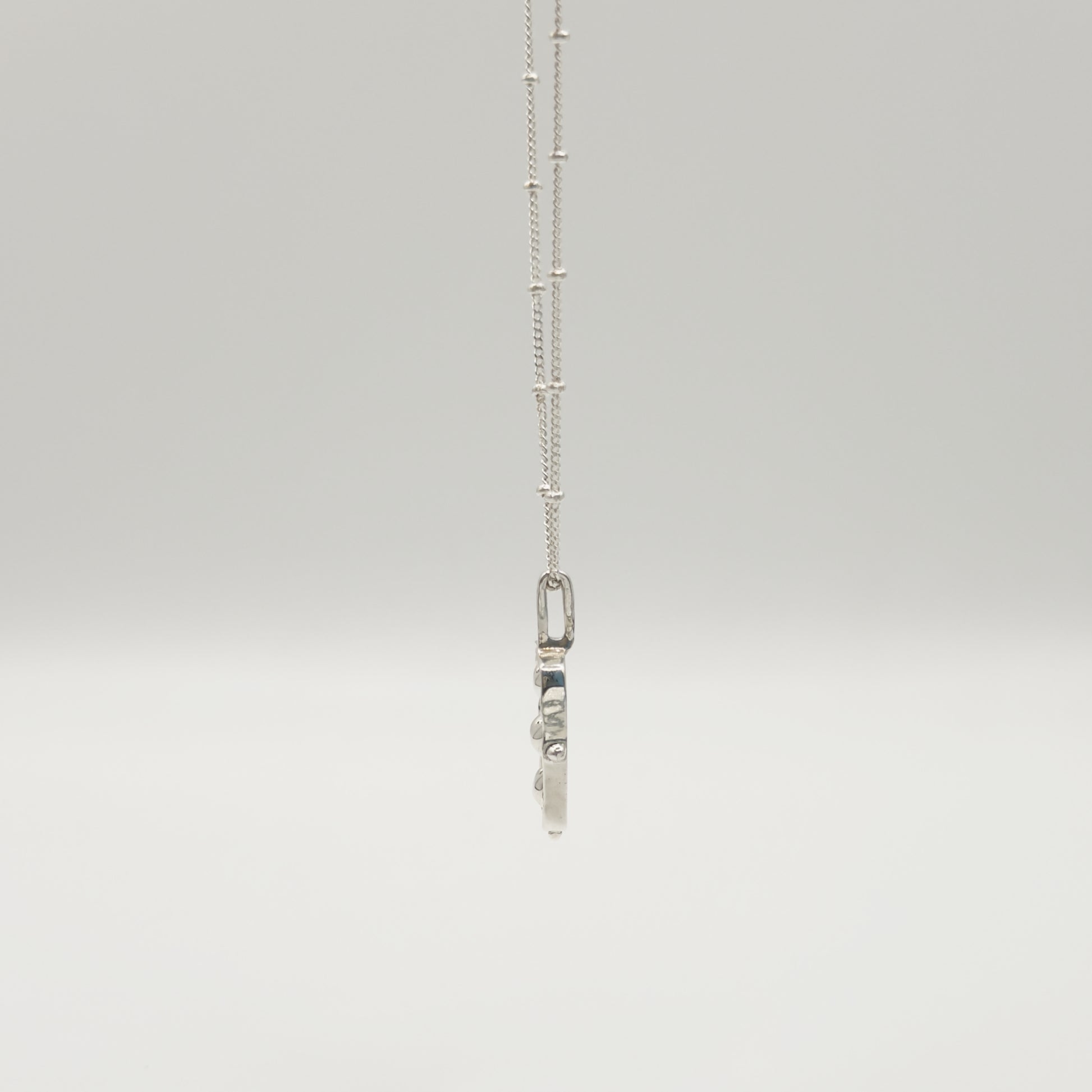 Side view of the Self-Compassion textured silver pendant on a satellite chain, pictured on a light plain background.