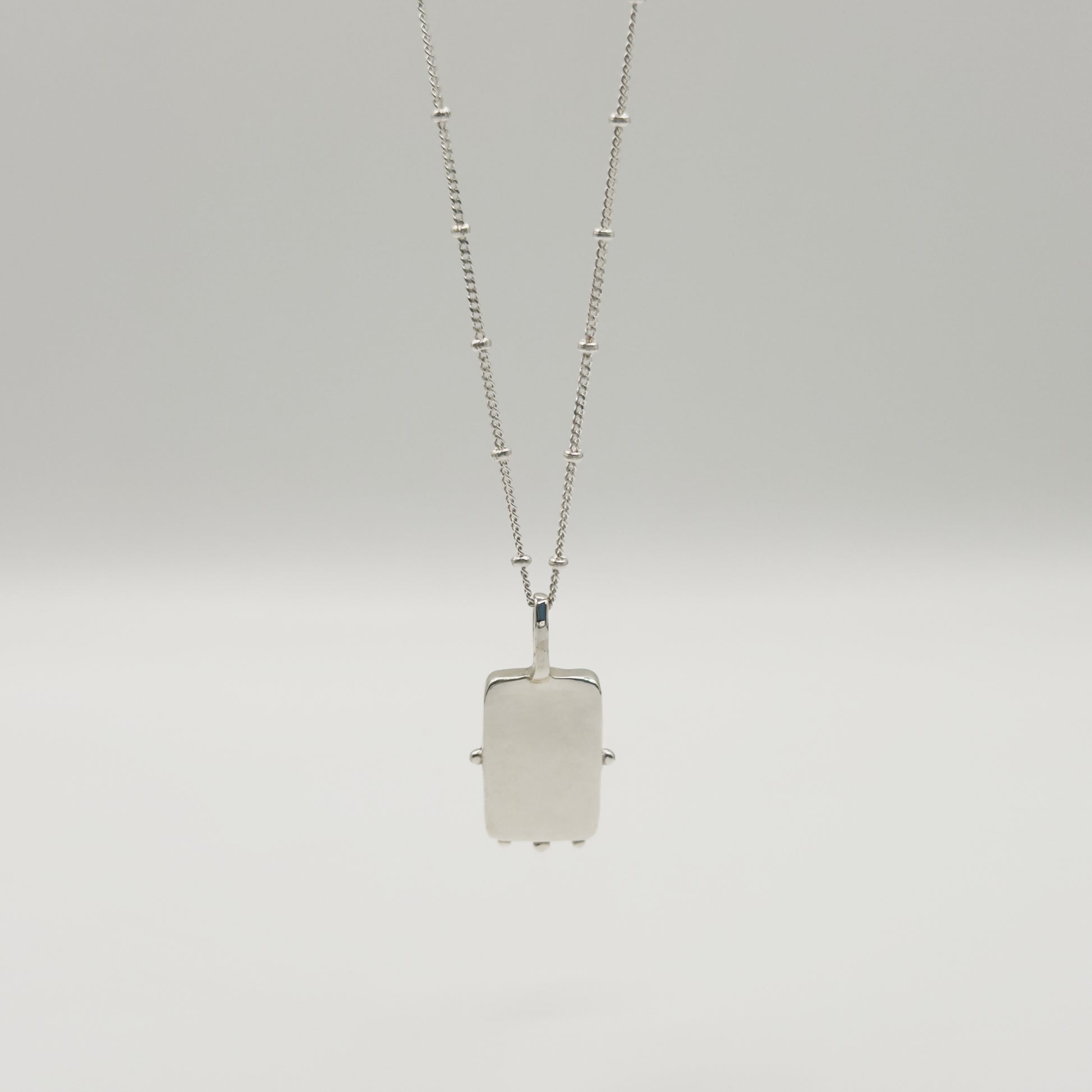 Back view of the Self-Compassion textured silver pendant on a satellite chain, pictured on a light plain background.