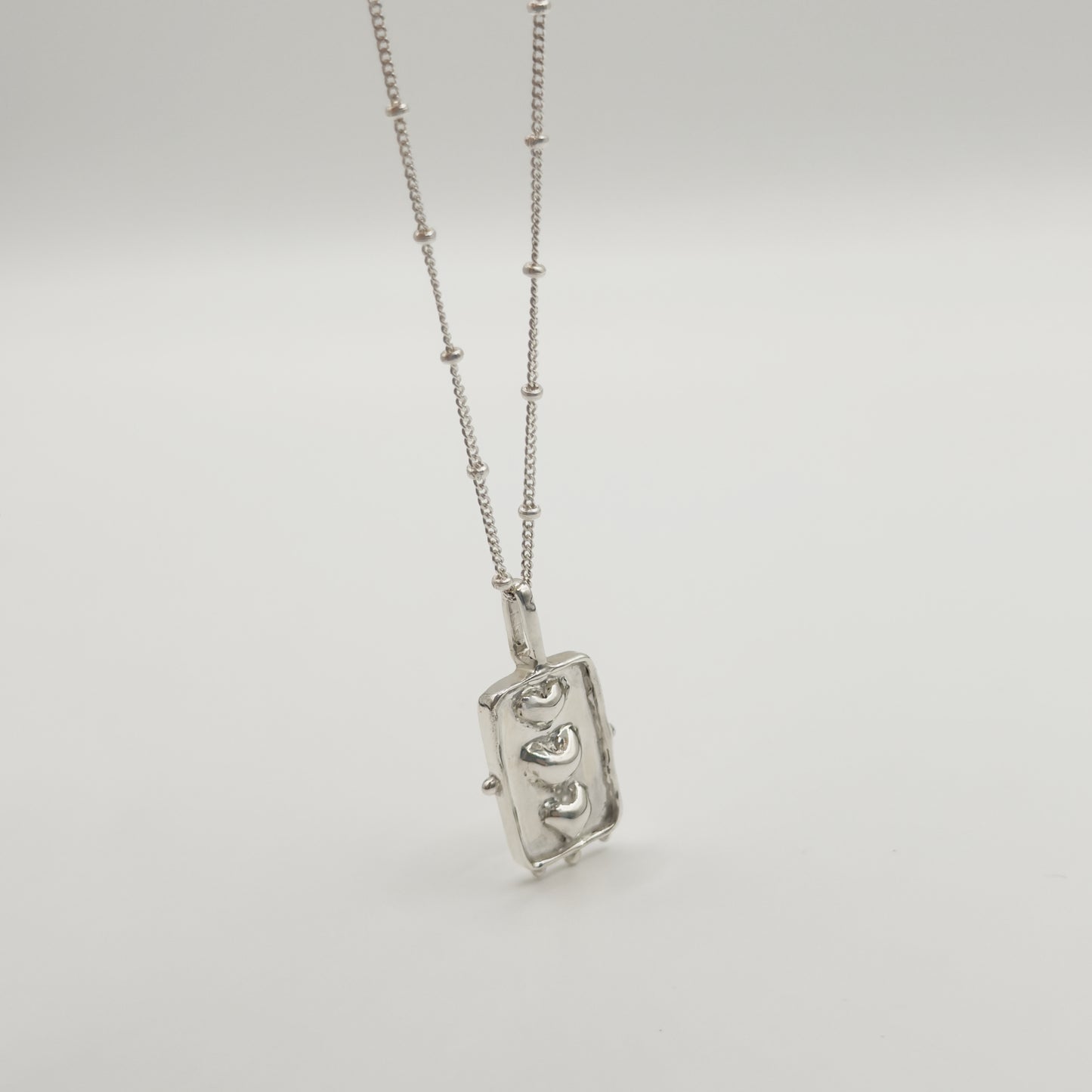 Angled front view of the Self-Compassion textured silver pendant on a satellite chain, pictured on a light plain background.
