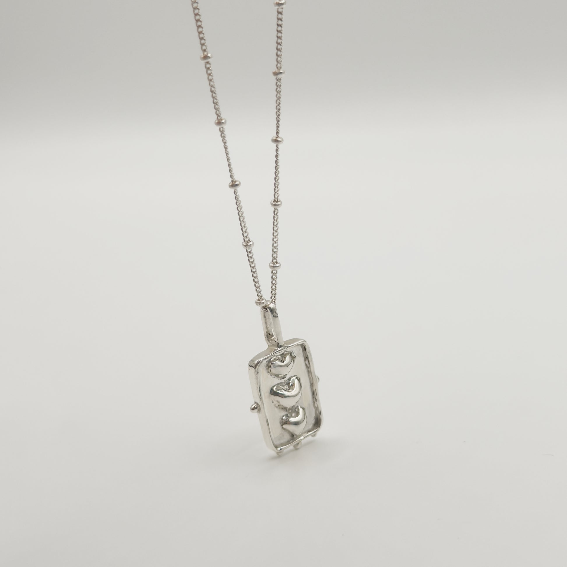 Angled front view of the Self-Compassion textured silver pendant on a satellite chain, pictured on a light plain background.