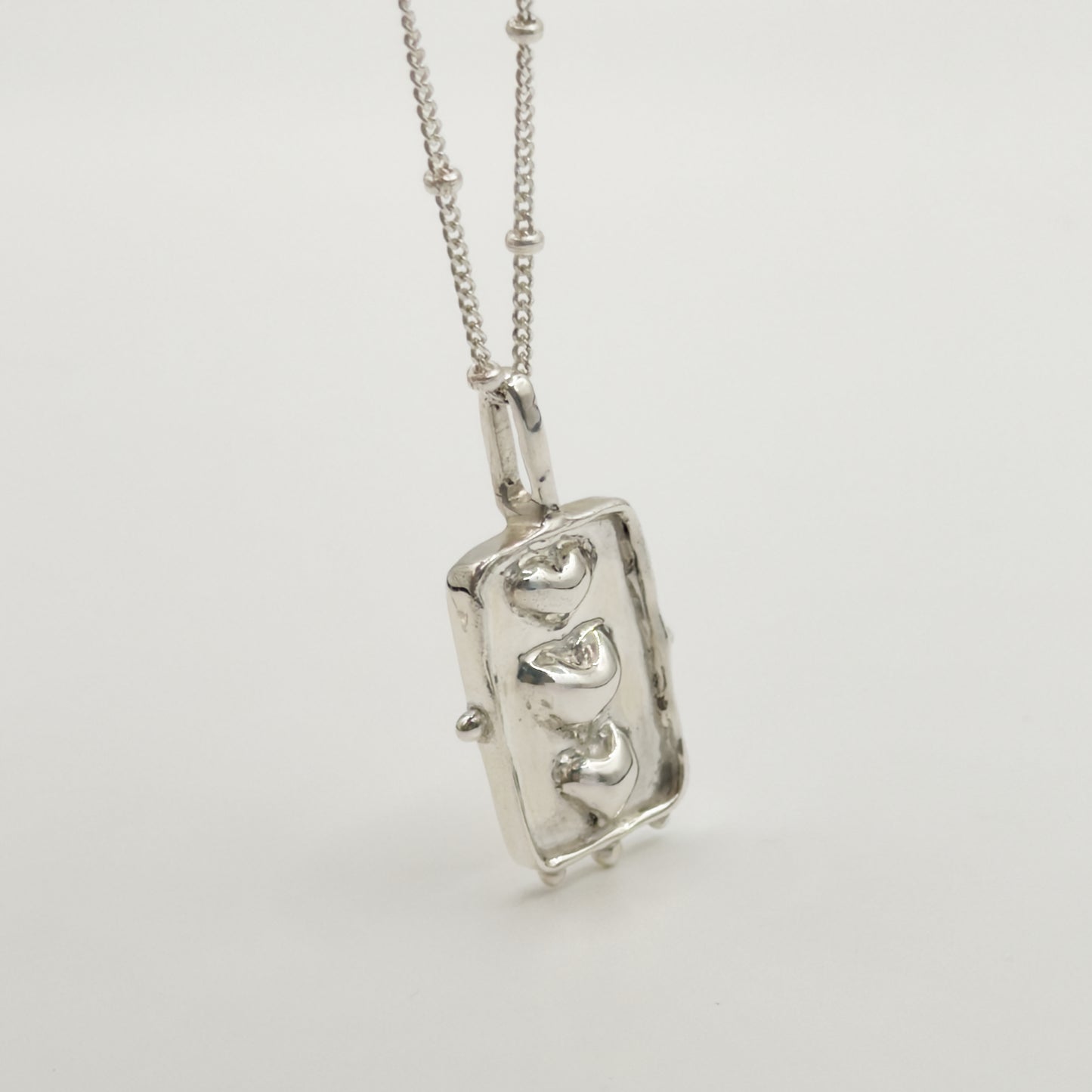 Close-up view of the Self-Compassion textured silver pendant on a satellite chain, pictured on a light plain background.