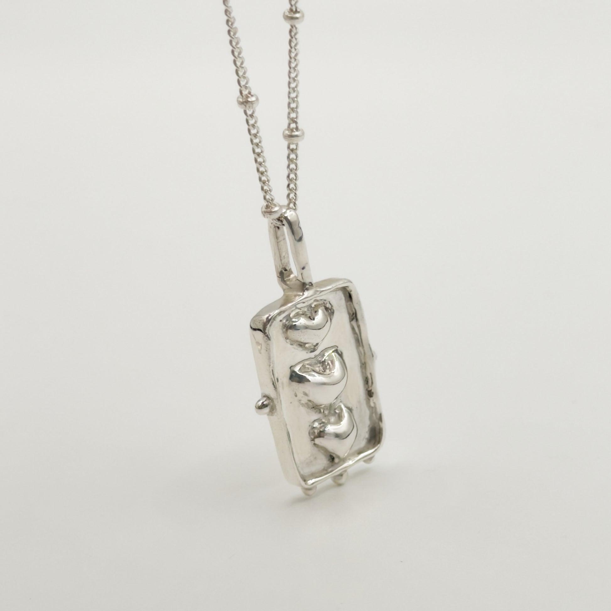 Close-up view of the Self-Compassion textured silver pendant on a satellite chain, pictured on a light plain background.