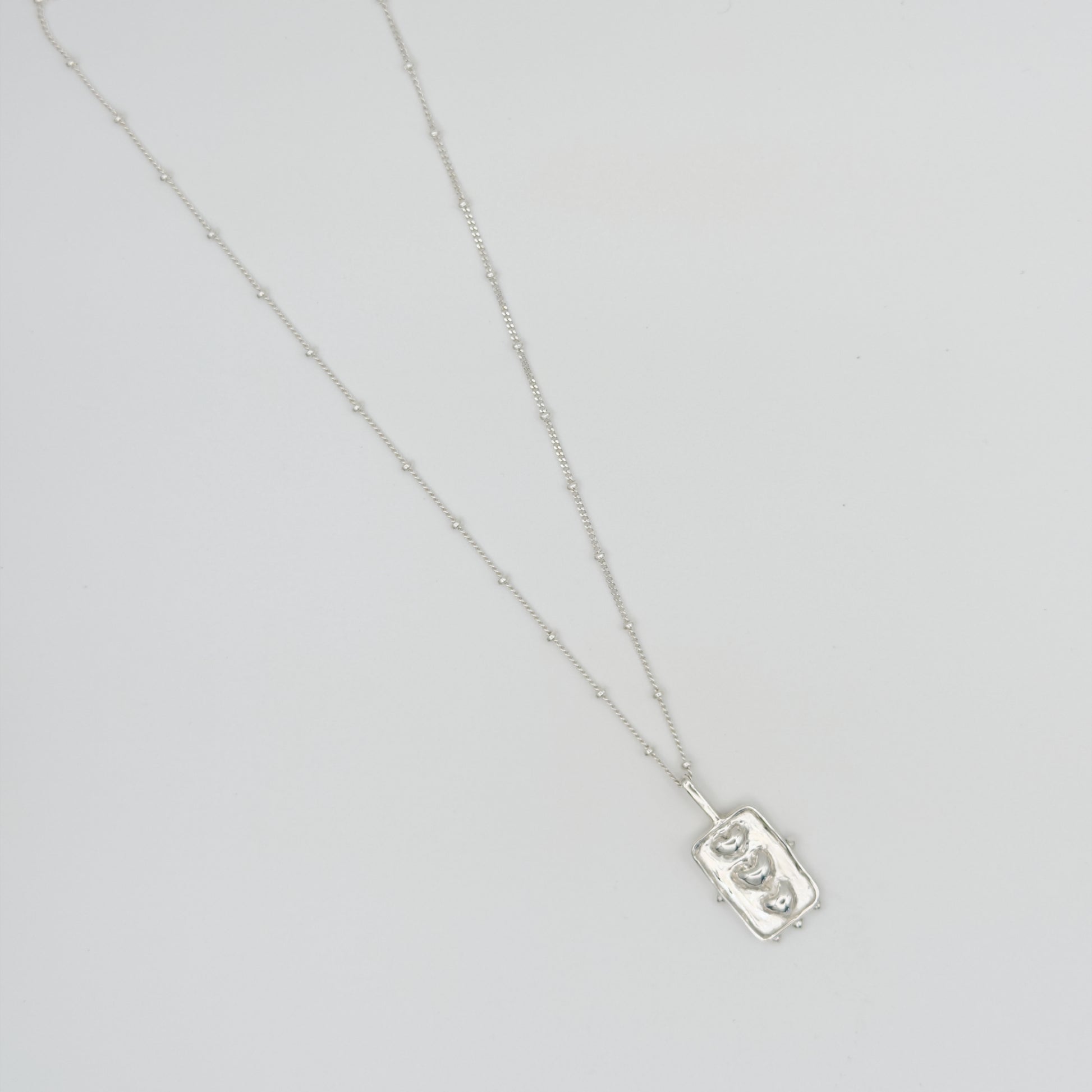 Top view of the Self-Compassion textured silver pendant on a satellite chain, pictured on a light plain background.