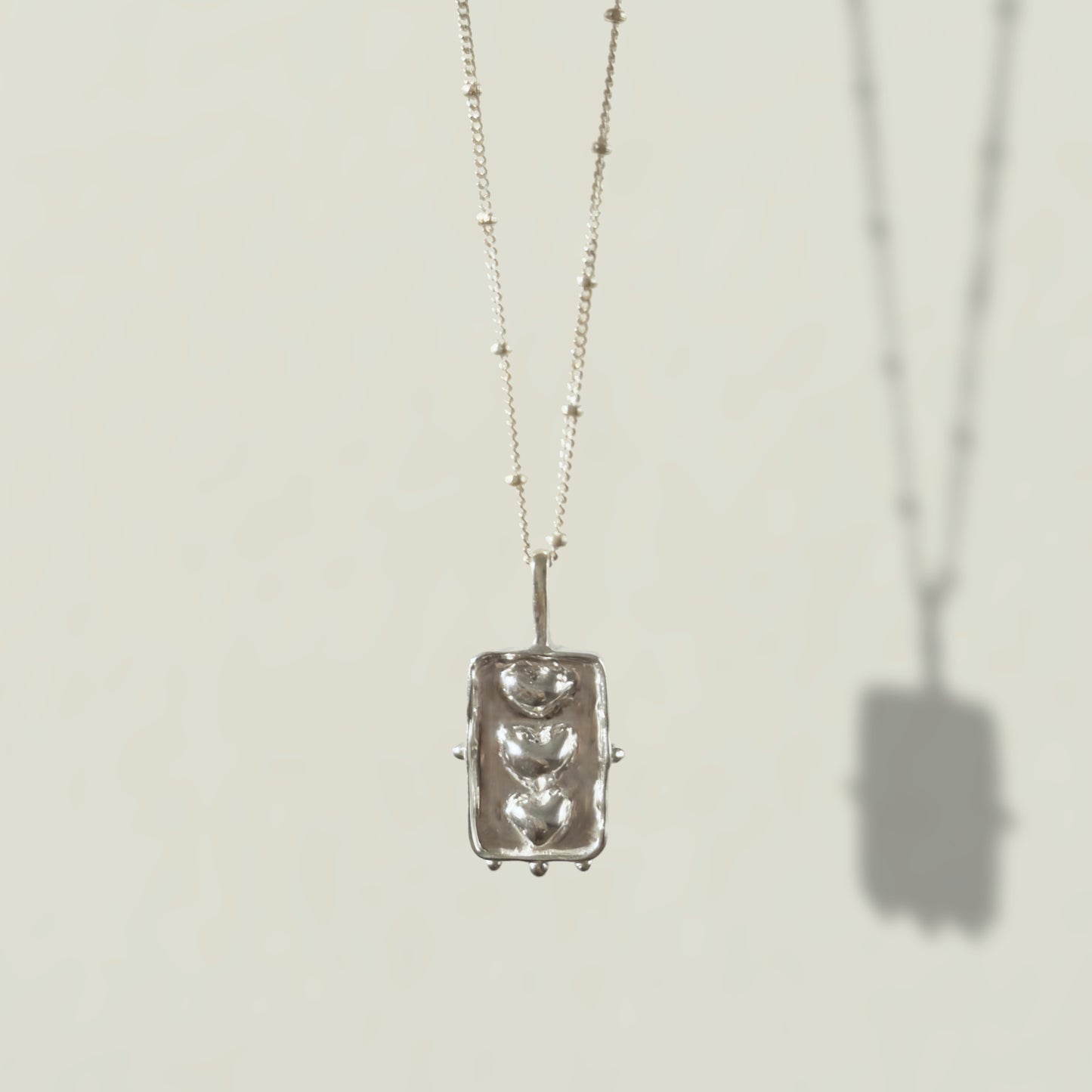 Front view of the Self-Compassion textured silver pendant on a satellite chain, pictured on a light plain background.