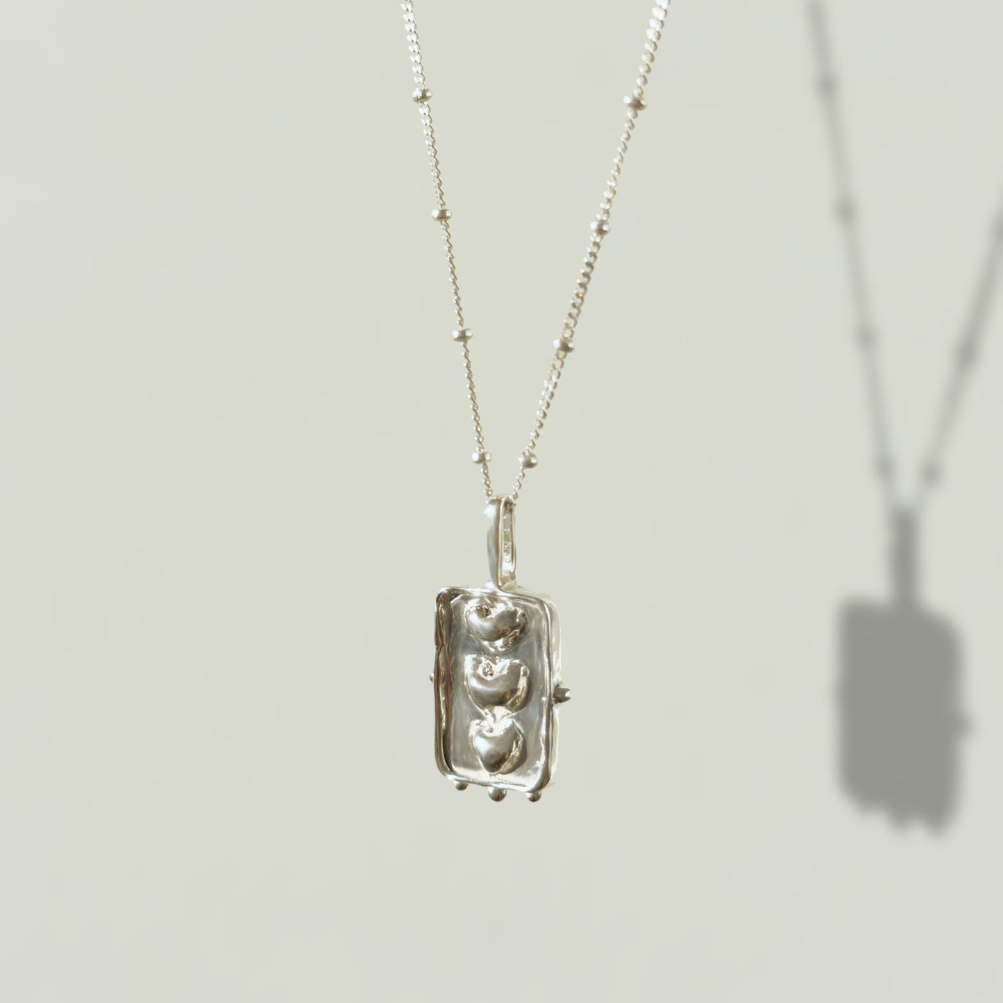 Angled front view of the Self-Compassion textured silver pendant on a satellite chain, pictured on a light plain background.
