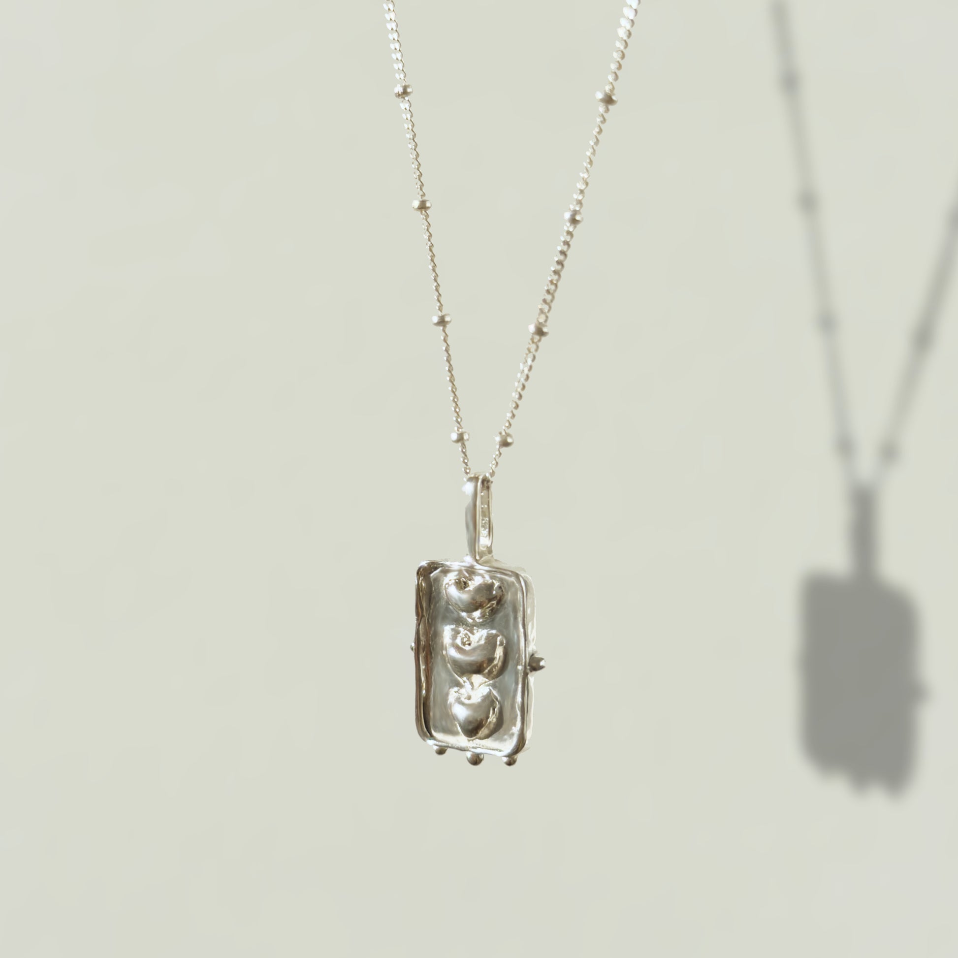 Angled front view of the Self-Compassion textured silver pendant on a satellite chain, pictured on a light plain background.