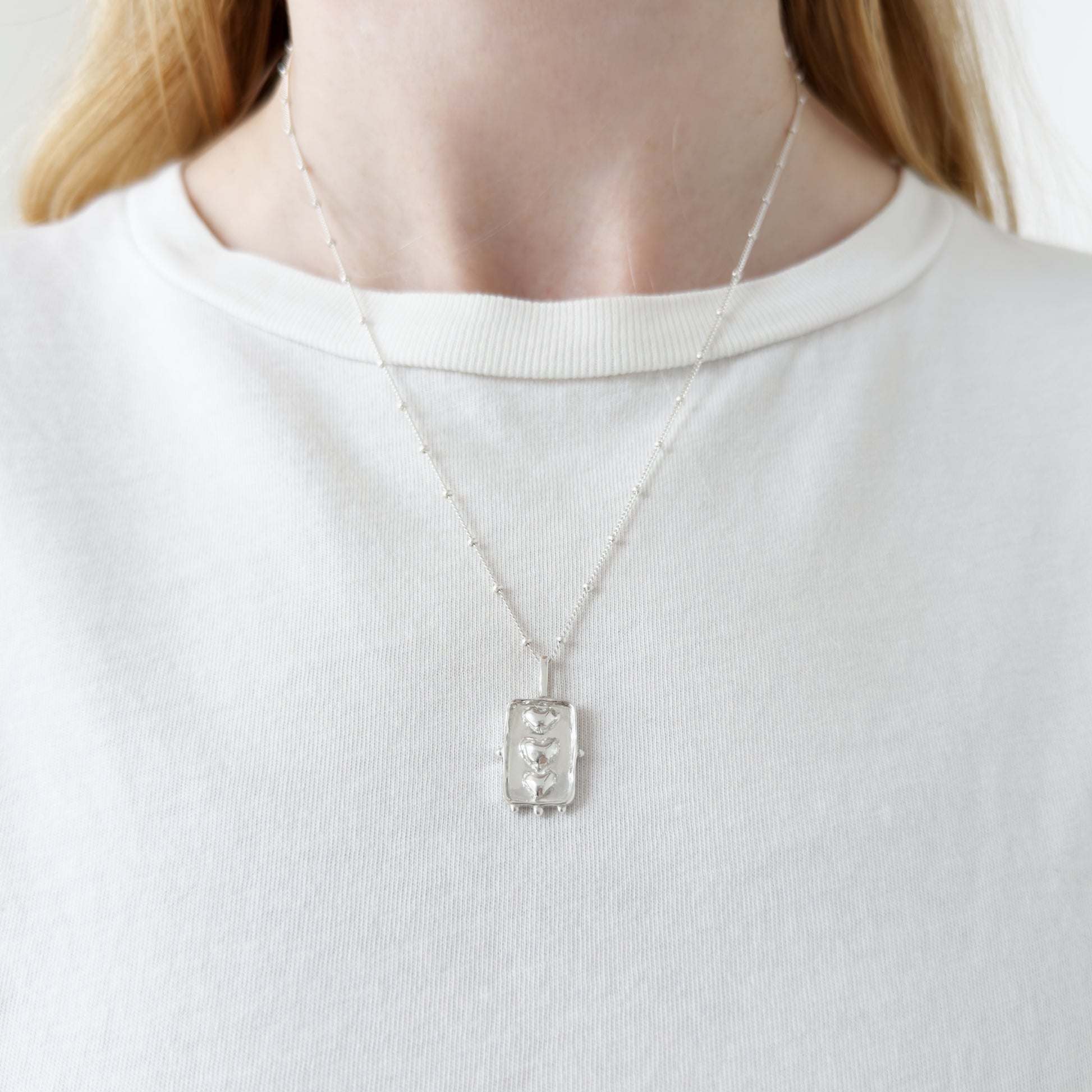 Self-Compassion textured silver pendant on a satellite chain. Pictured on a person wearing a white top.