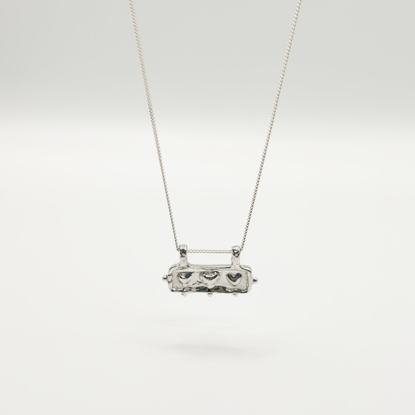 Front view of the Self-Love textured silver pendant on a curb chain, pictured on a light plain background.