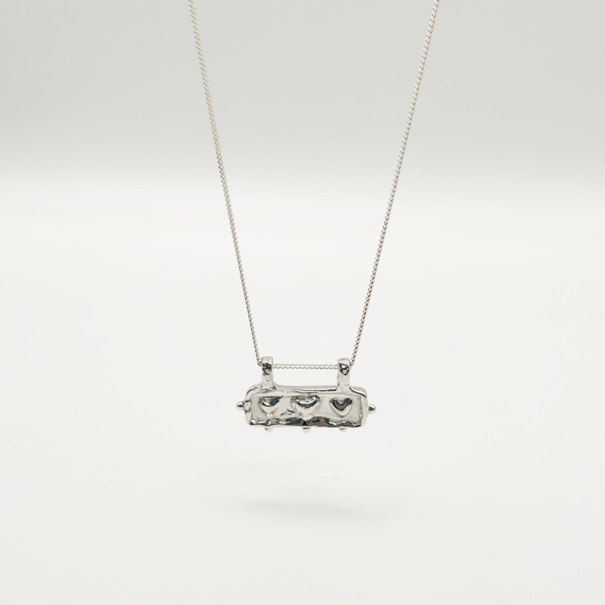 Front view of the Self-Love textured silver pendant on a curb chain, pictured on a light plain background.
