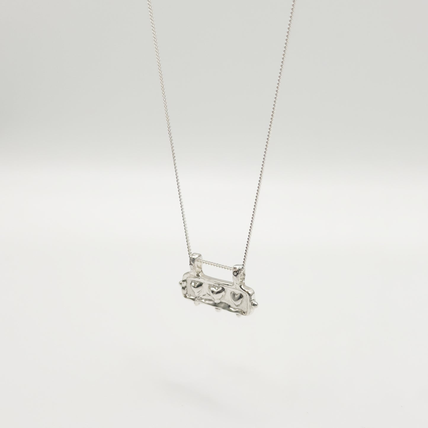 Angled front view of the Self-Love textured silver pendant on a curb chain, pictured on a light plain background.