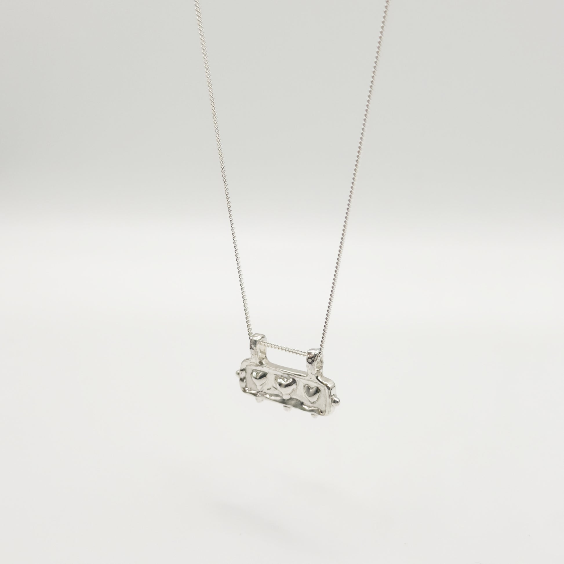 Angled front view of the Self-Love textured silver pendant on a curb chain, pictured on a light plain background.