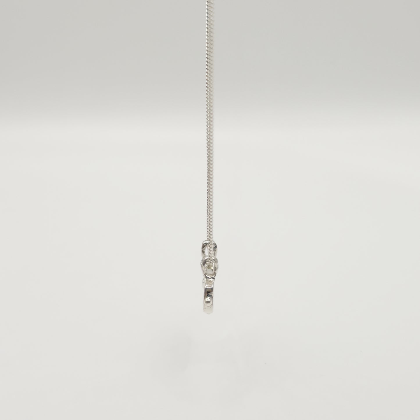 Side view of the Self-Love textured silver pendant on a curb chain, pictured on a light plain background.