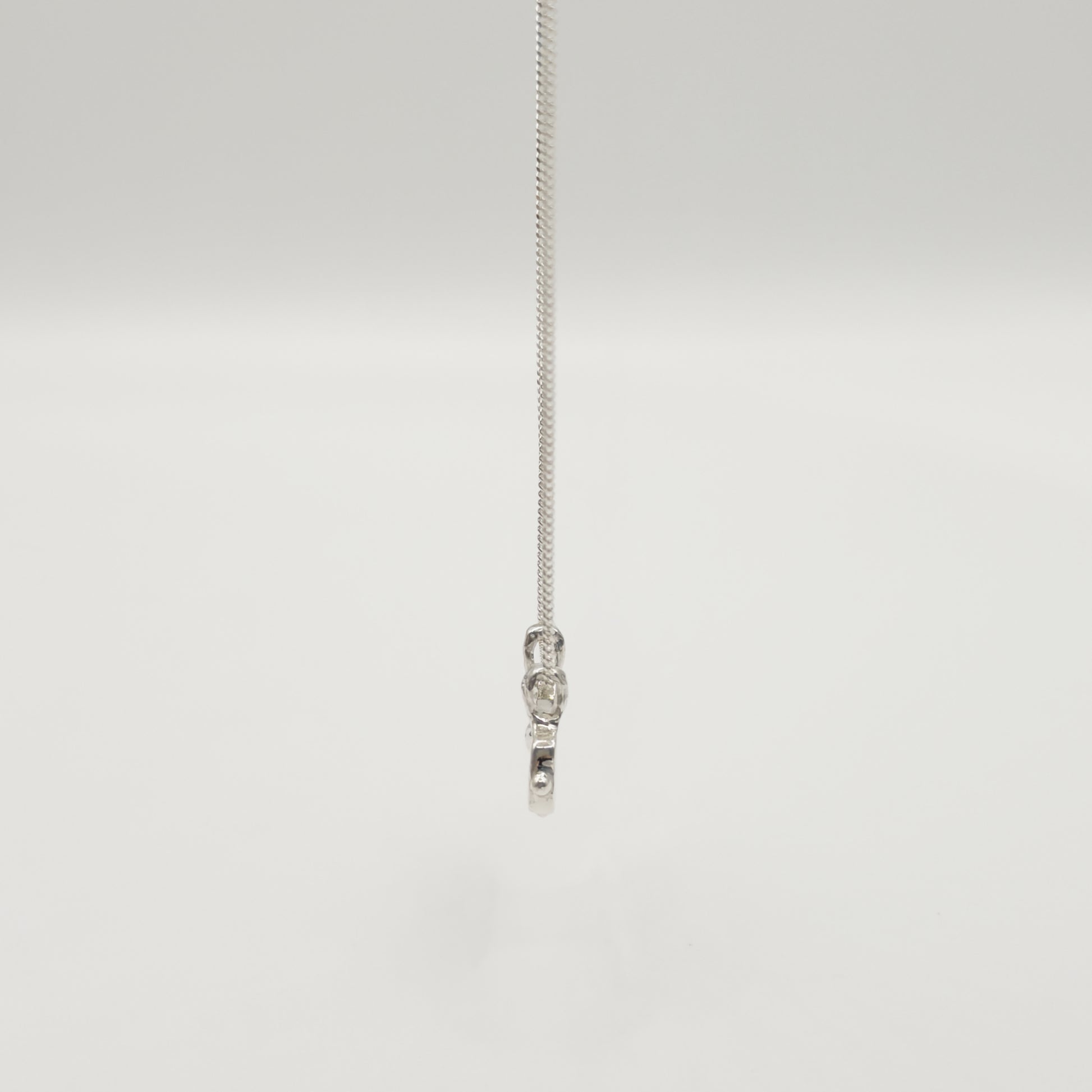 Side view of the Self-Love textured silver pendant on a curb chain, pictured on a light plain background.