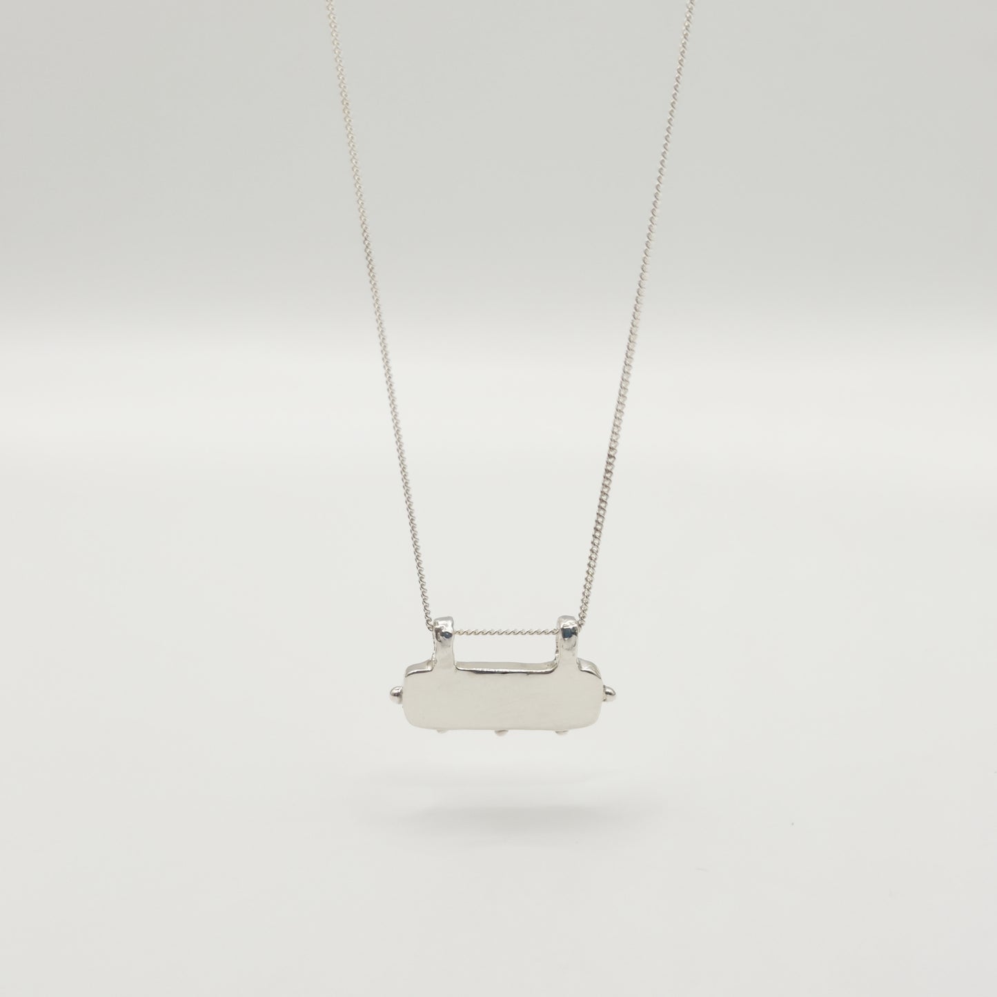 Back view of the Self-Love textured silver pendant on a curb chain, pictured on a light plain background.
