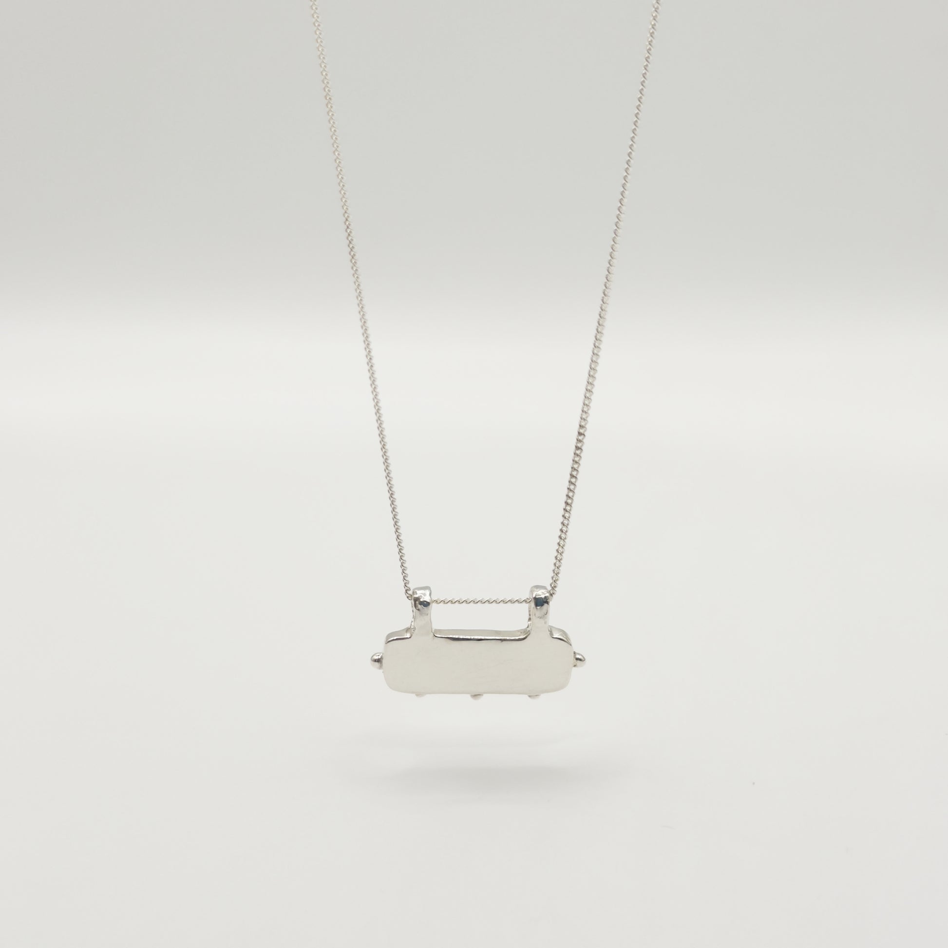 Back view of the Self-Love textured silver pendant on a curb chain, pictured on a light plain background.