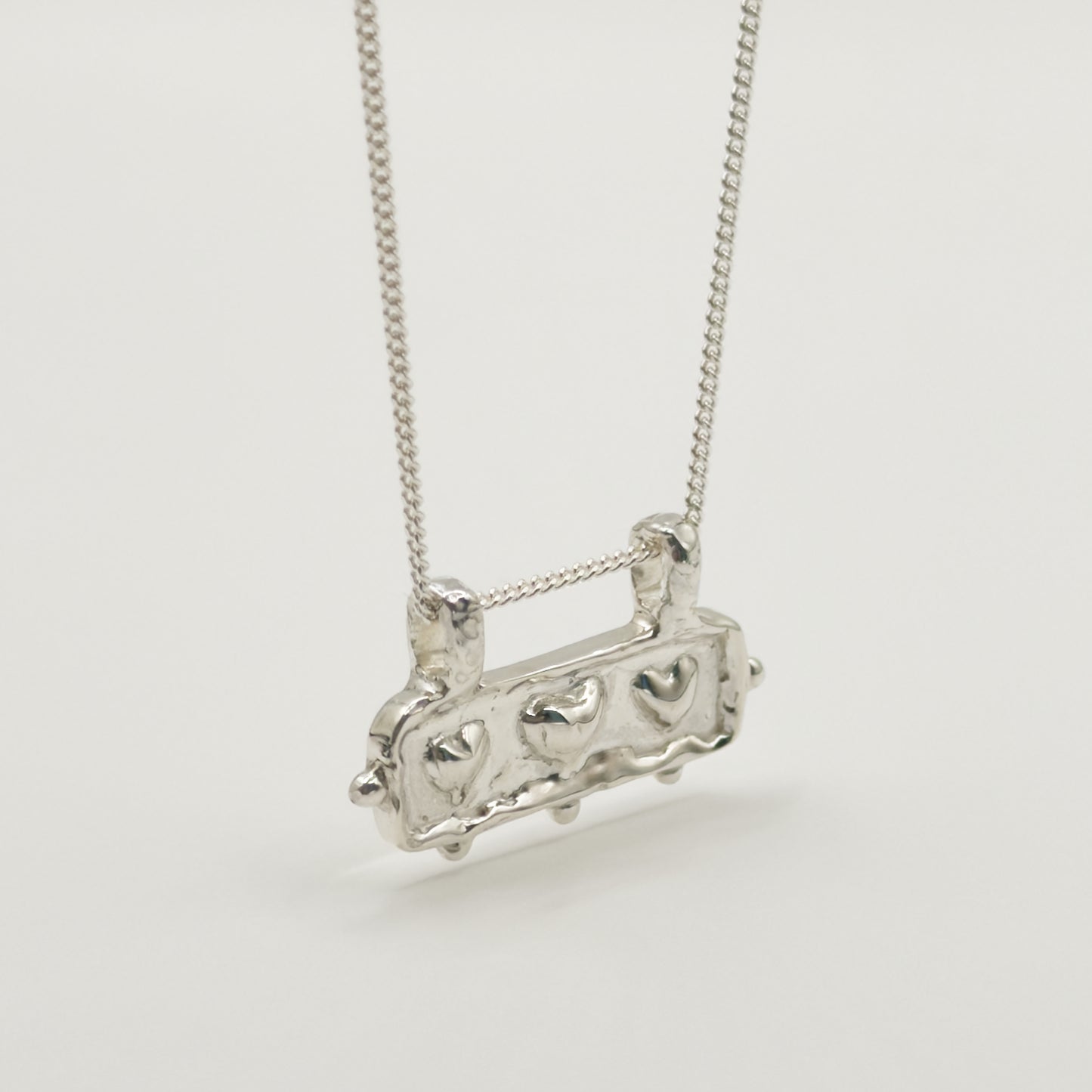 Close-up view of the Self-Love textured silver pendant on a curb chain, pictured on a light plain background.
