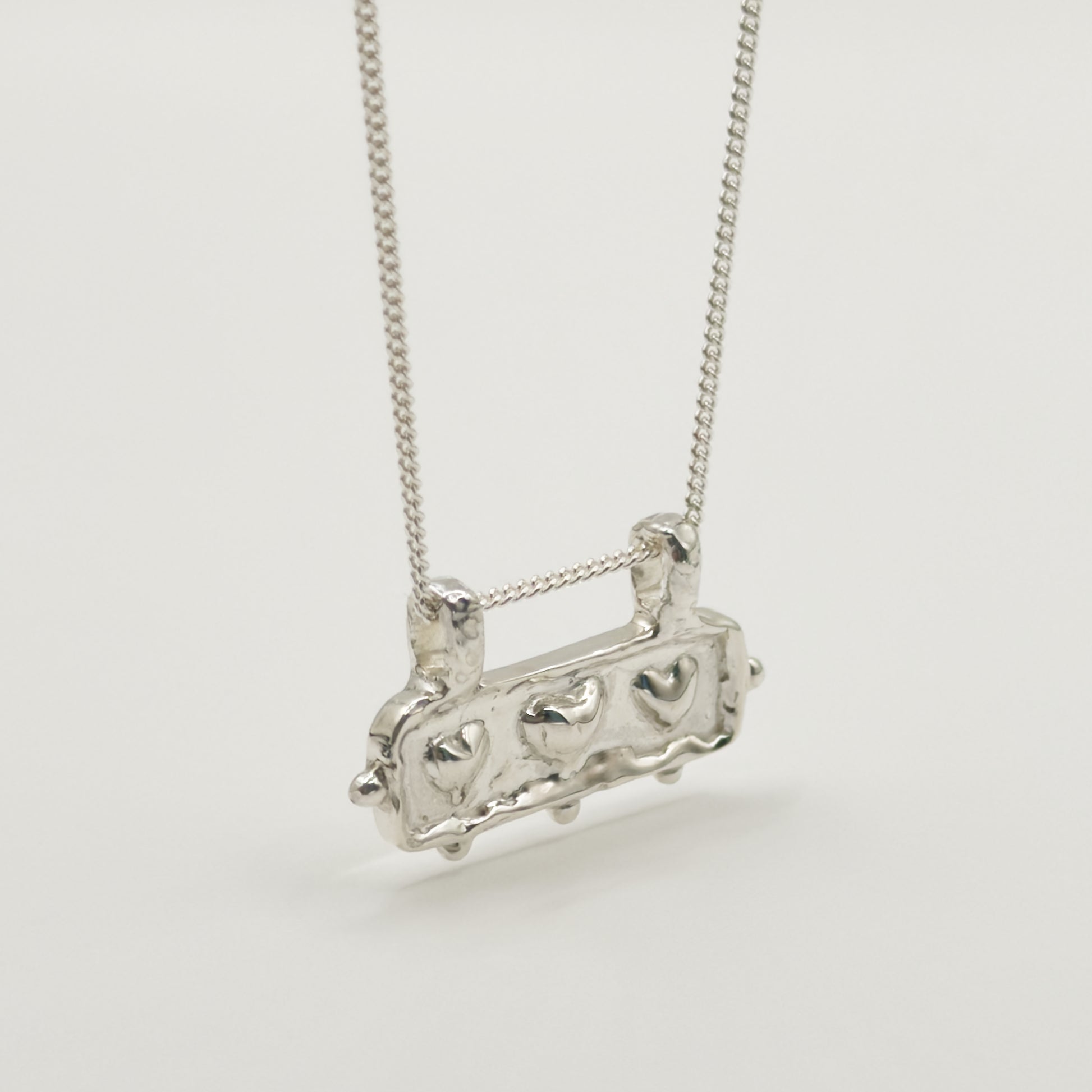 Close-up view of the Self-Love textured silver pendant on a curb chain, pictured on a light plain background.