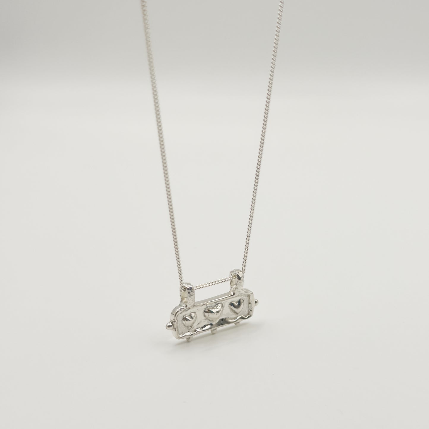 Angled front view of the Self-Love textured silver pendant on a curb chain, pictured on a light plain background.
