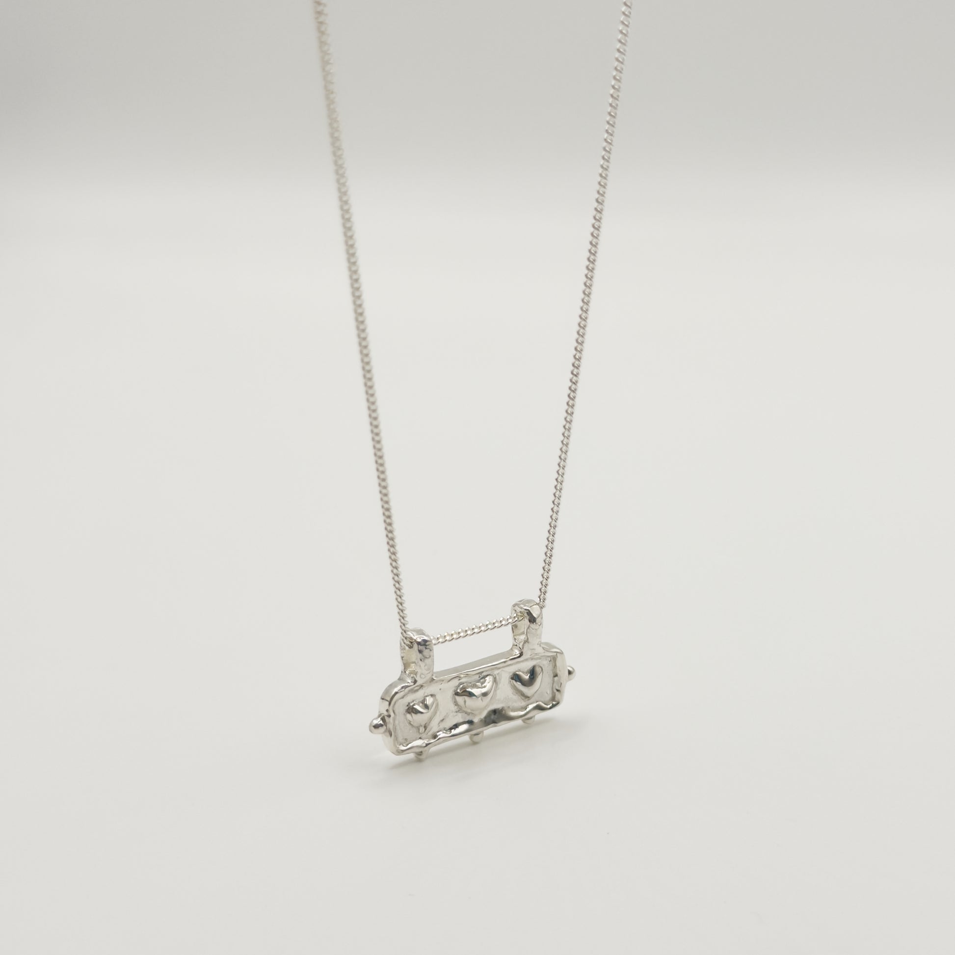Angled front view of the Self-Love textured silver pendant on a curb chain, pictured on a light plain background.