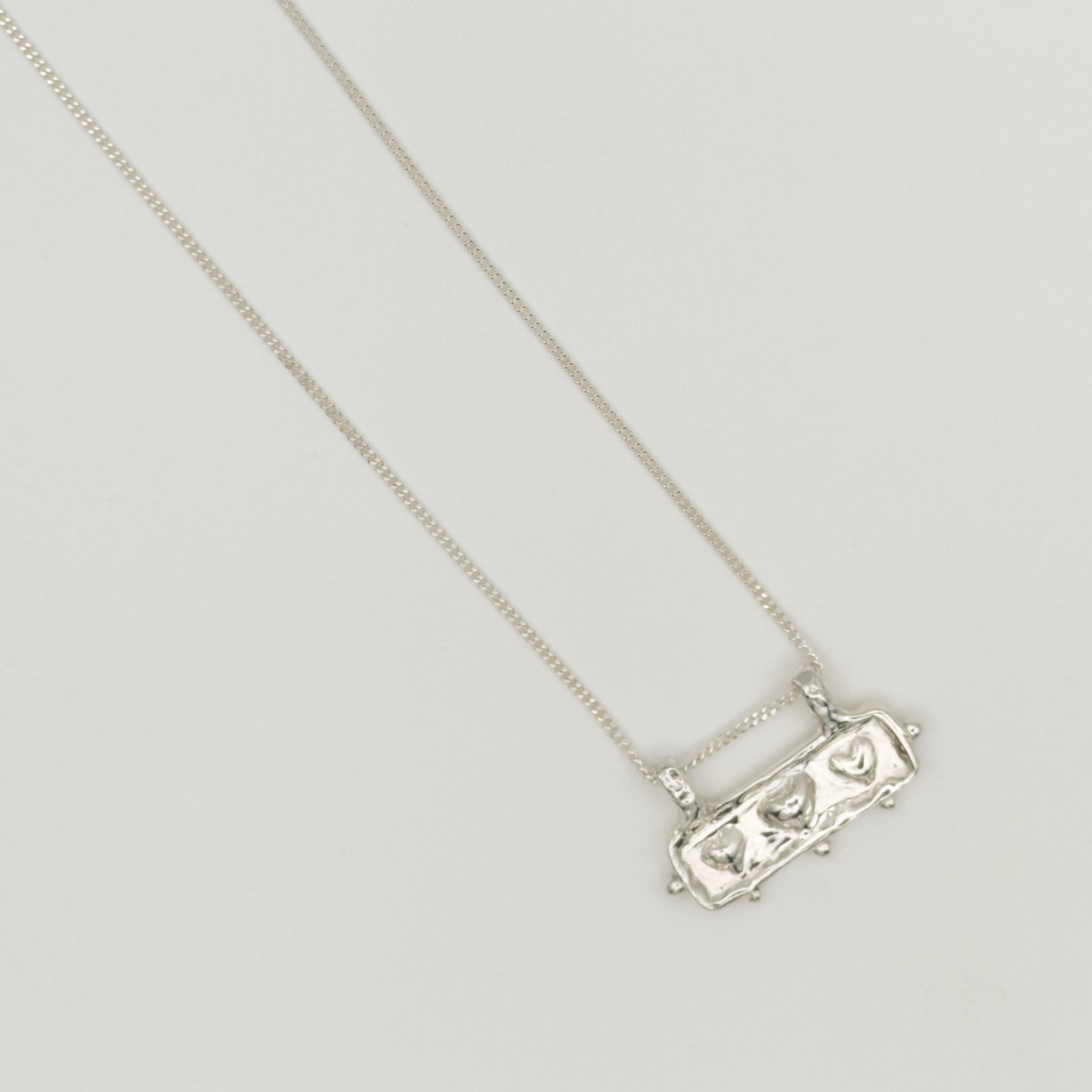 Close-up top view of the Self-Love textured silver pendant on a curb chain, pictured on a light plain background.