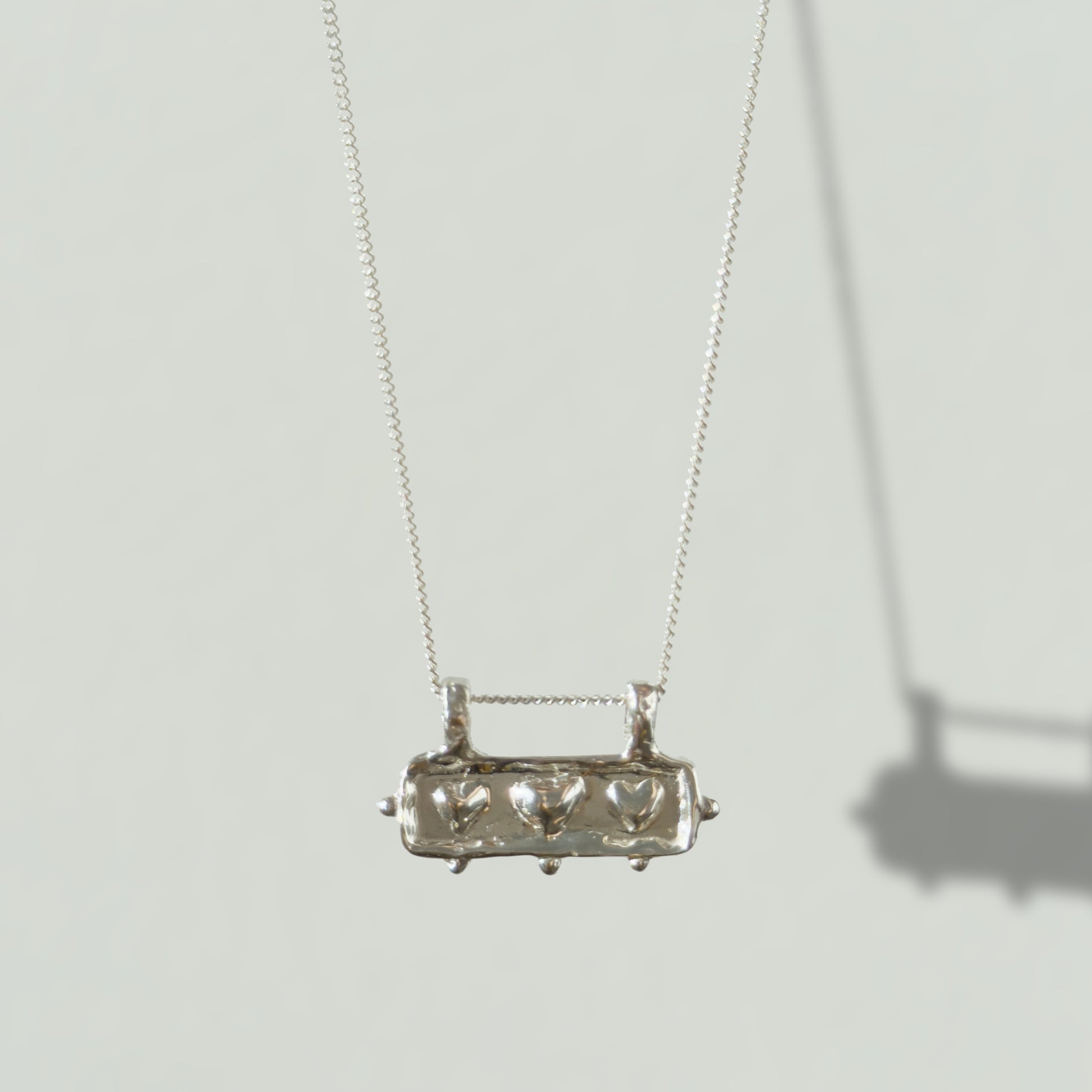 Front view of the Self-Love textured silver pendant on a curb chain, pictured on a light plain background.