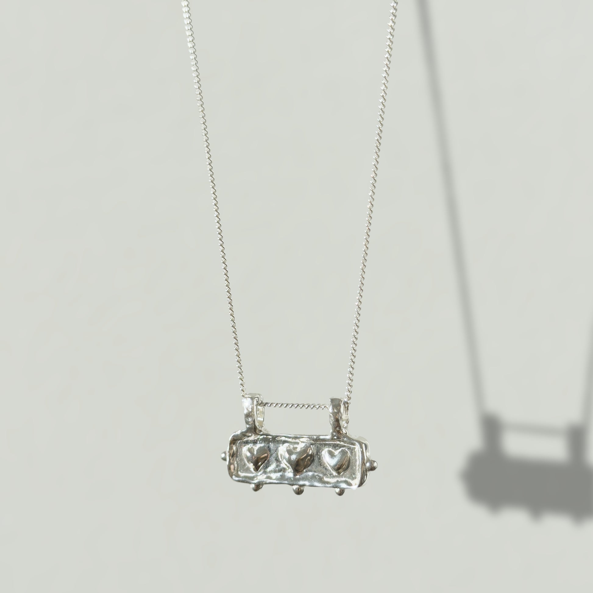 Angled front view of the Self-Love textured silver pendant on a curb chain, pictured on a light plain background.