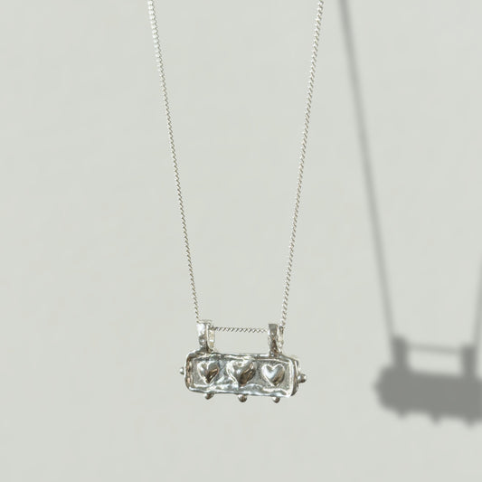 Angled front view of the Self-Love textured silver pendant on a curb chain, pictured on a light plain background.