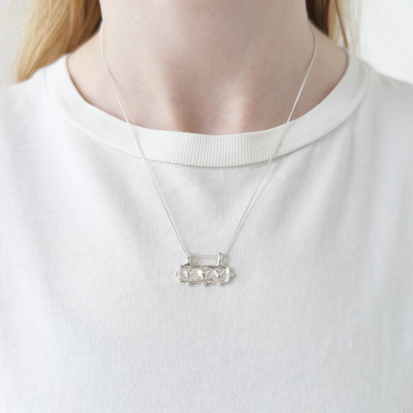 Self-Love textured silver pendant on a curb chain. Pictured on a person wearing a white top.