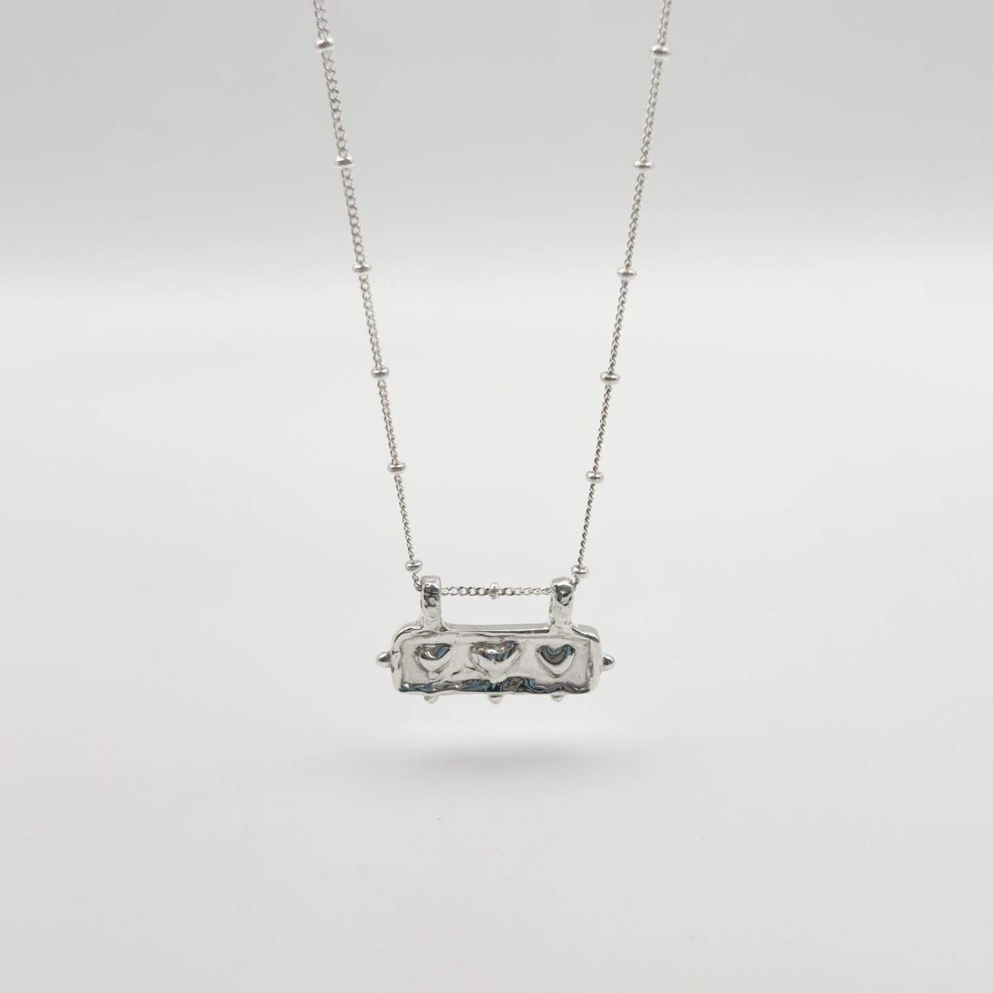 Front view of the Self-Love textured silver pendant on a satellite chain, pictured on a light plain background.
