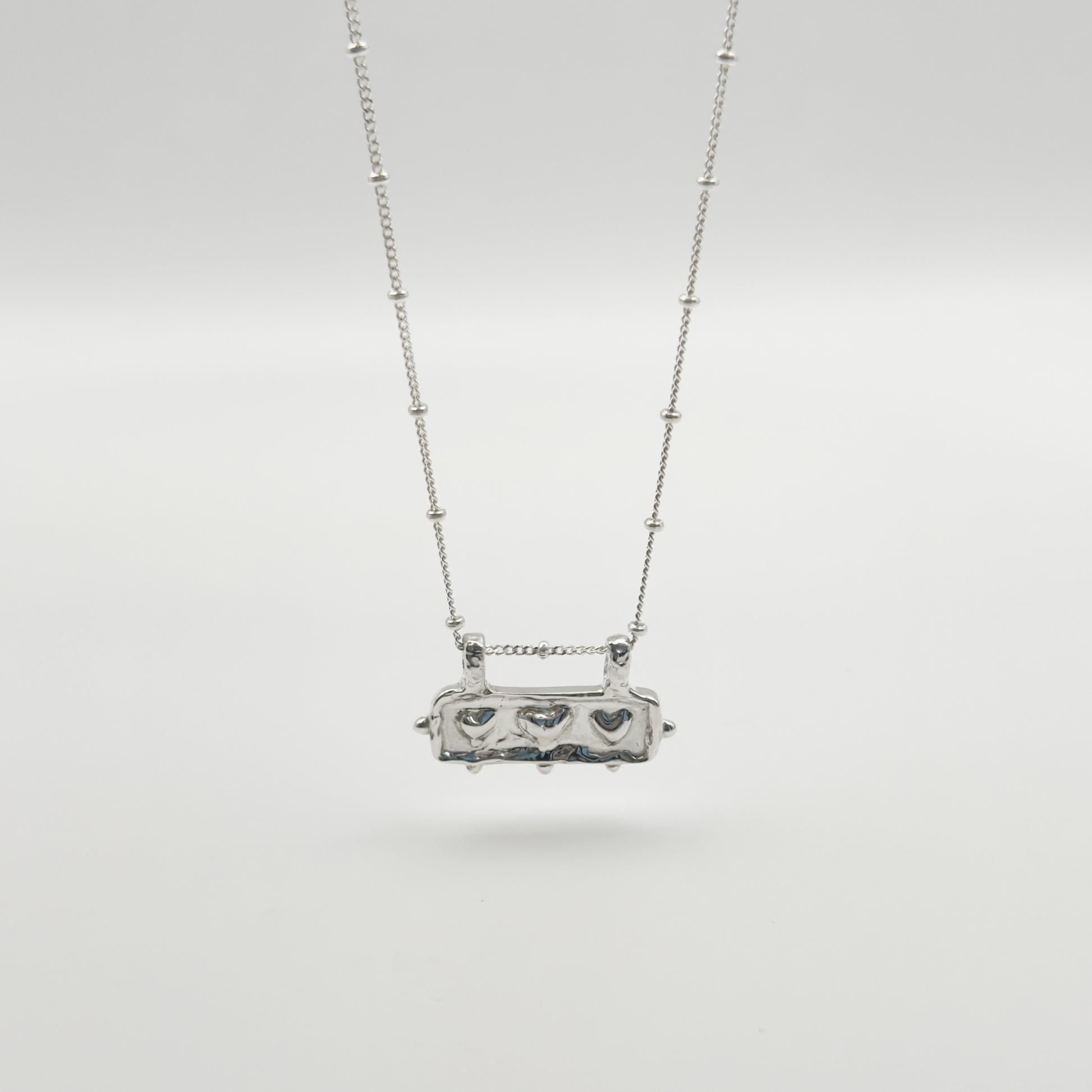 Front view of the Self-Love textured silver pendant on a satellite chain, pictured on a light plain background.