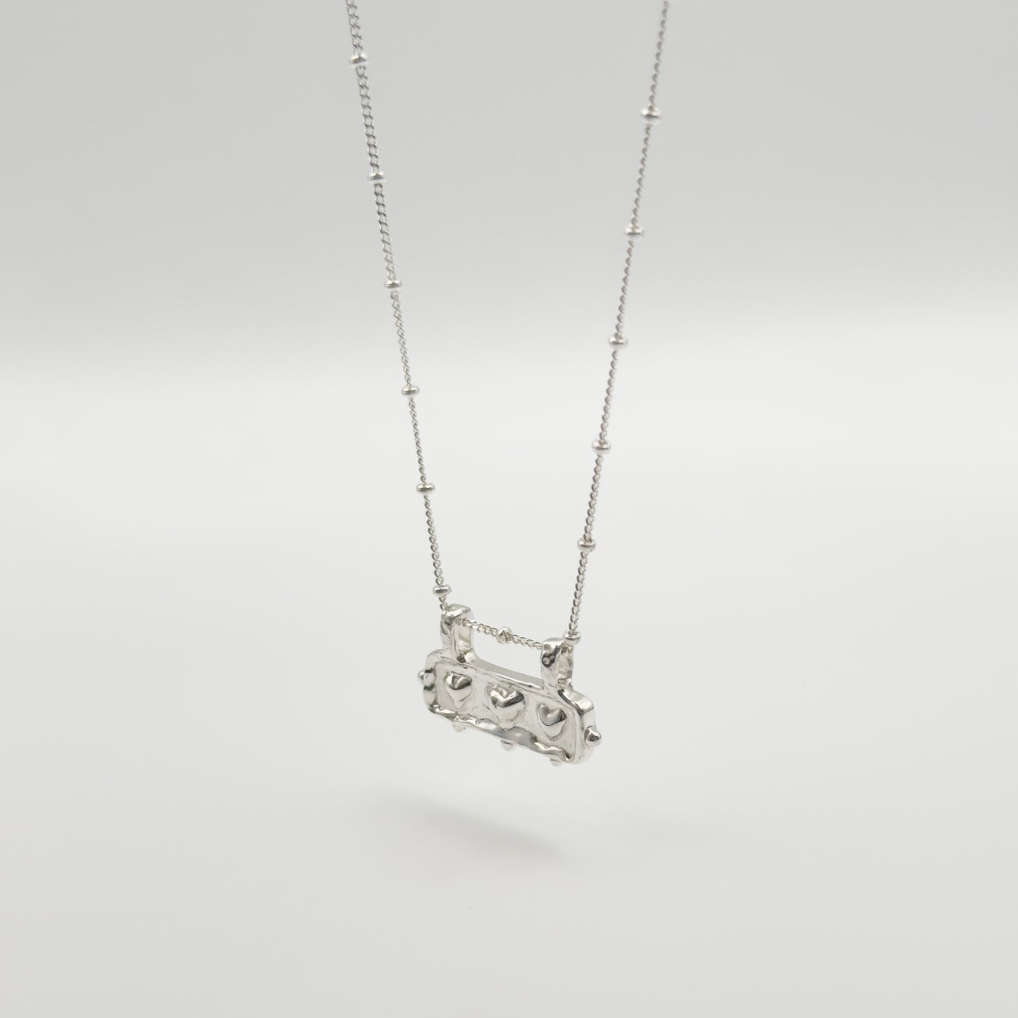 Angled front view of the Self-Love textured silver pendant on a satellite chain, pictured on a light plain background.