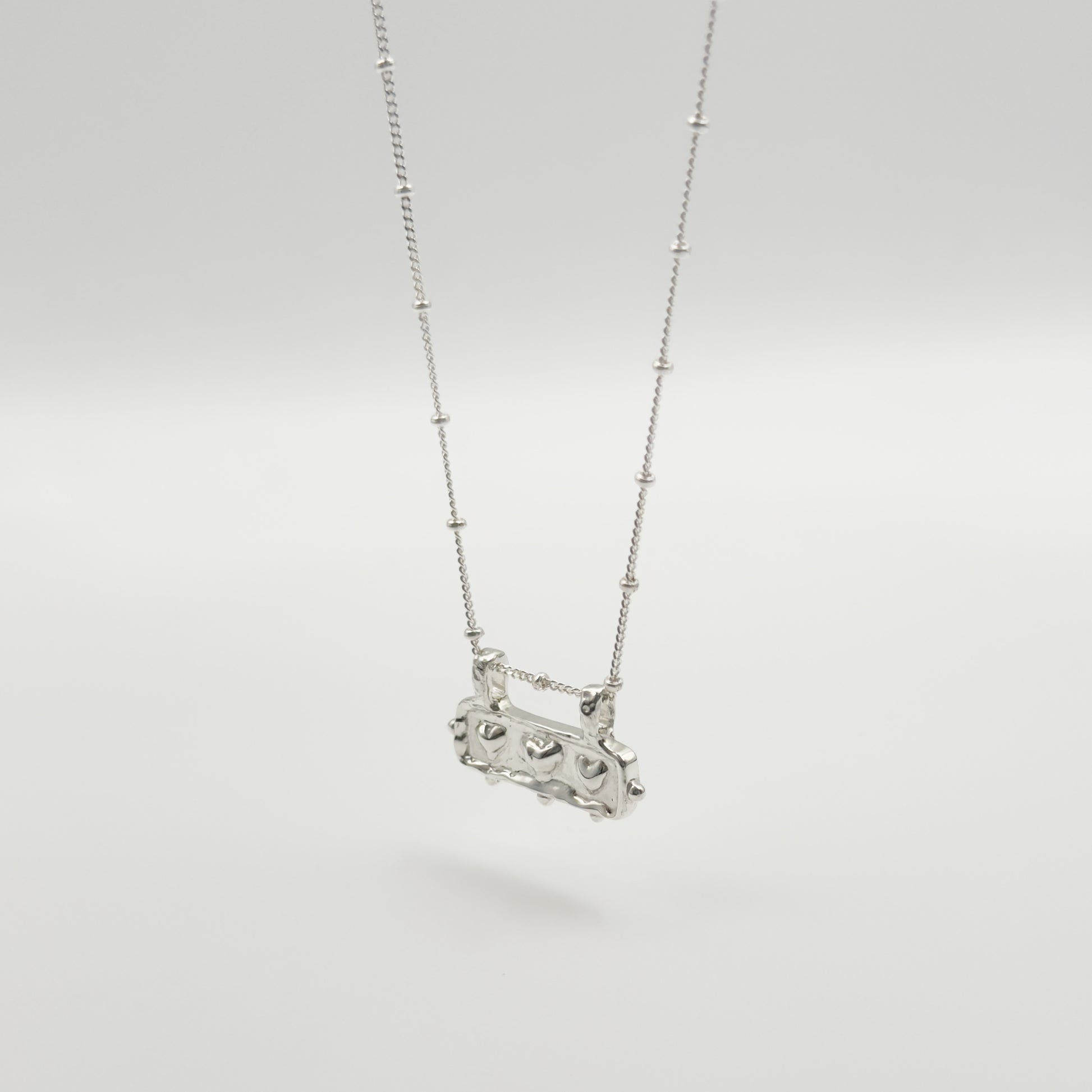 Angled front view of the Self-Love textured silver pendant on a satellite chain, pictured on a light plain background.