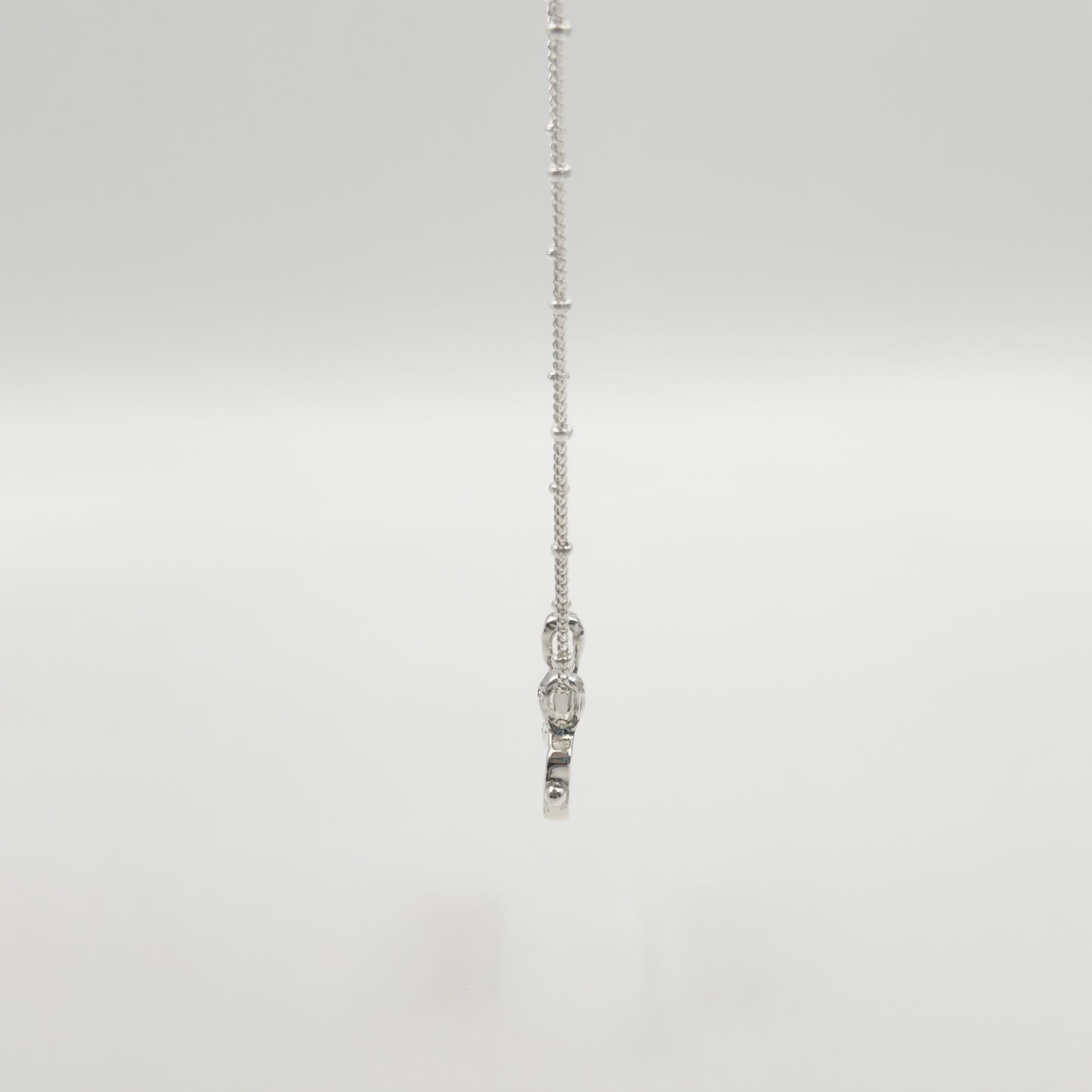 Side view of the Self-Love textured silver pendant on a satellite chain, pictured on a light plain background.