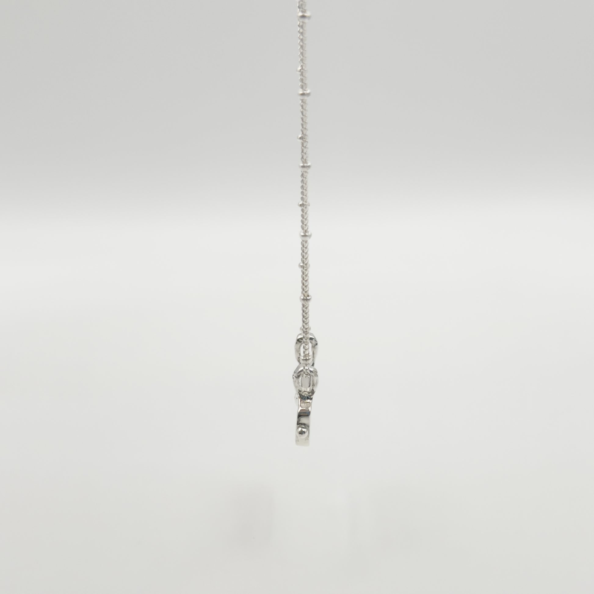 Side view of the Self-Love textured silver pendant on a satellite chain, pictured on a light plain background.