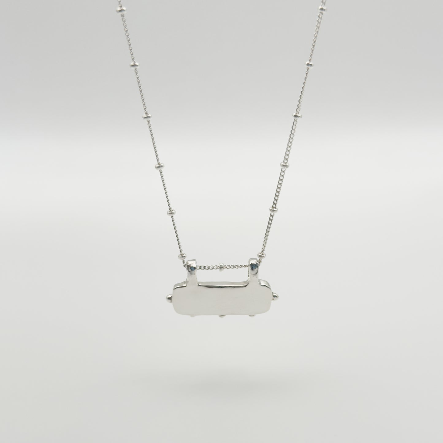 Back view of the Self-Love textured silver pendant on a satellite chain, pictured on a light plain background.