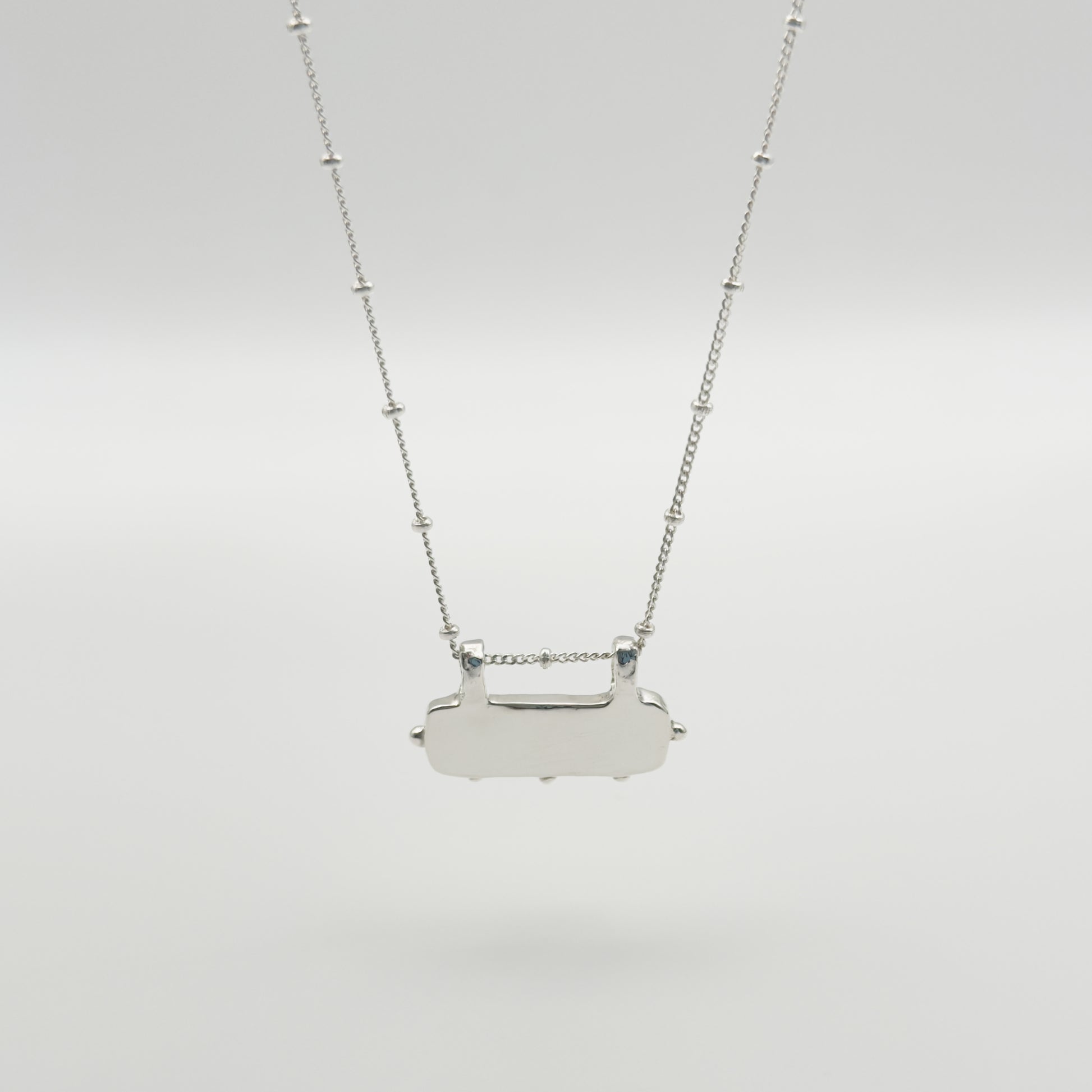 Back view of the Self-Love textured silver pendant on a satellite chain, pictured on a light plain background.